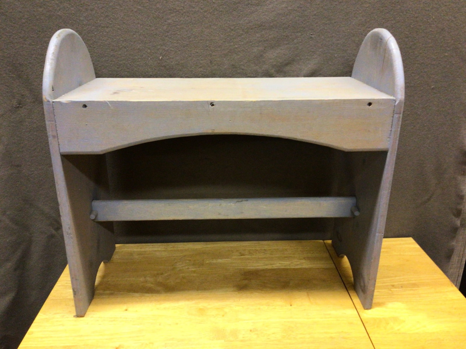 Handcrafted Wooden Bench With Blue Finish: This is a handcrafted wooden bench featuring a blue-painted finish. It is rectangular in shape and includes curved side panels along with a stabilizing bar at the bottom. The bench measures