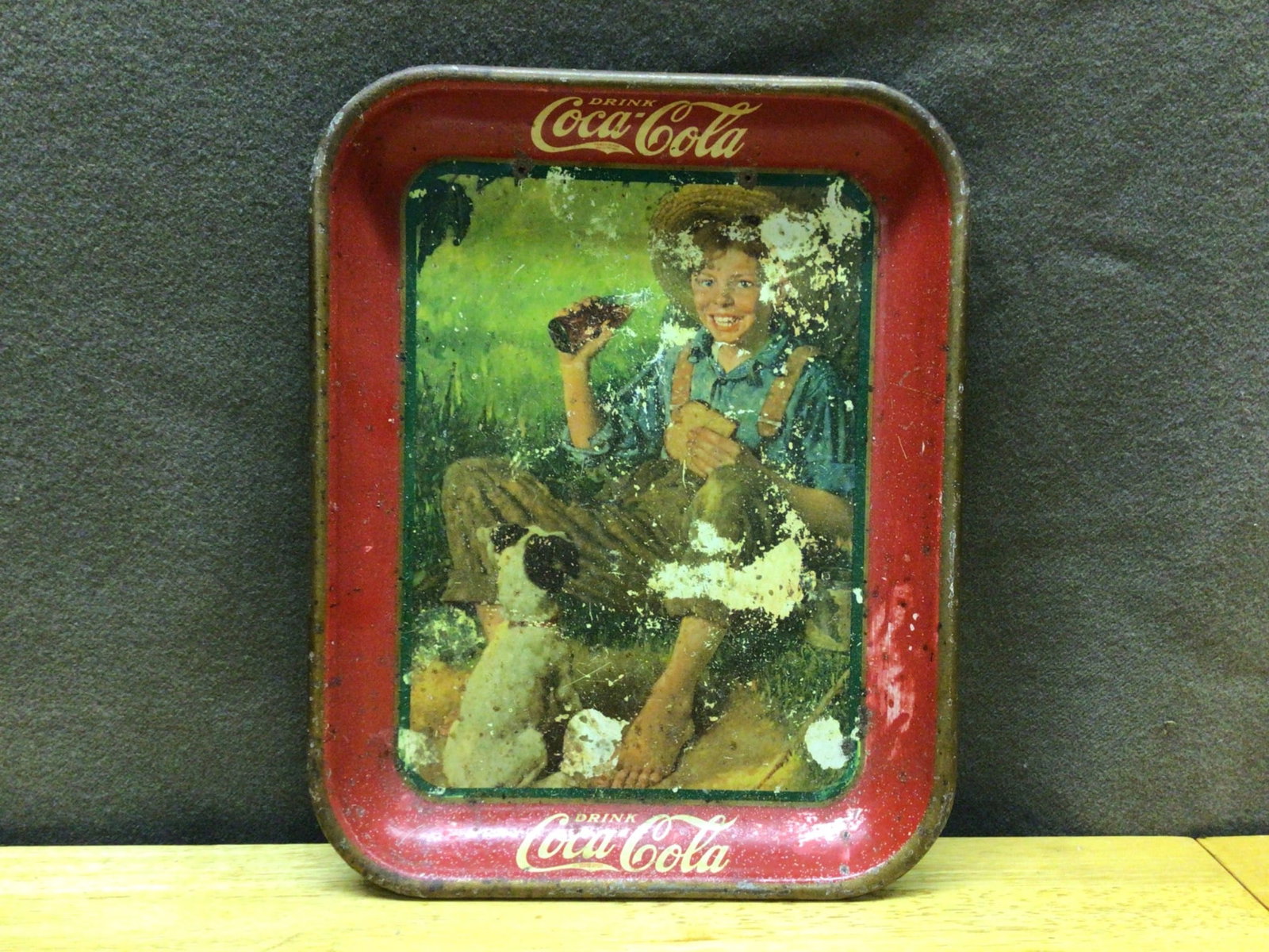 Original Paint Coca-Cola Drink Tray Featuring Boy with Bottle: This is an original Coca-Cola drink tray featuring a boy holding a Coca-Cola bottle. The tray shows significant paint wear and scratching consistent with its age and use. The lettering 'Drink Coca-Col