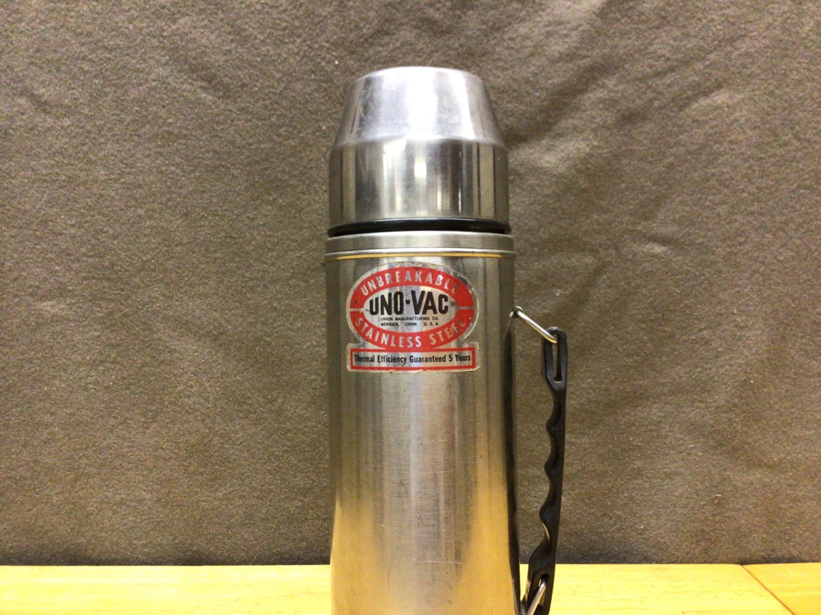 Uno-Vac Stainless Steel Thermos with Handle, Manufactured in Meriden, U.S.A.: Uno-Vac stainless steel thermos featuring a metal handle and screw-on cap that doubles as a cup. Embossed on the bottom with 'Uno-Vac' and 'Meriden Conn. U.S.A.' The thermos is made from unbreakable