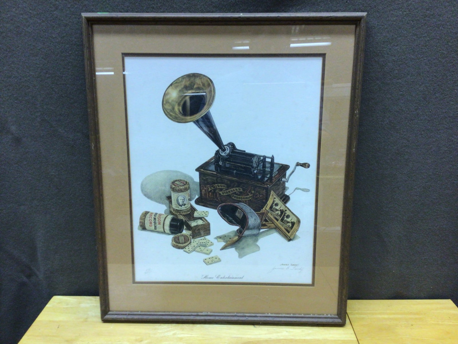 Framed Print 'Home Entertainment' by James B. Tardy 588/2000: This framed art print, numbered 588 of a limited series of 2000, is titled 'Home Entertainment' by James B. Tardy. The piece features a depiction of a phonograph and gaming pieces. The frame