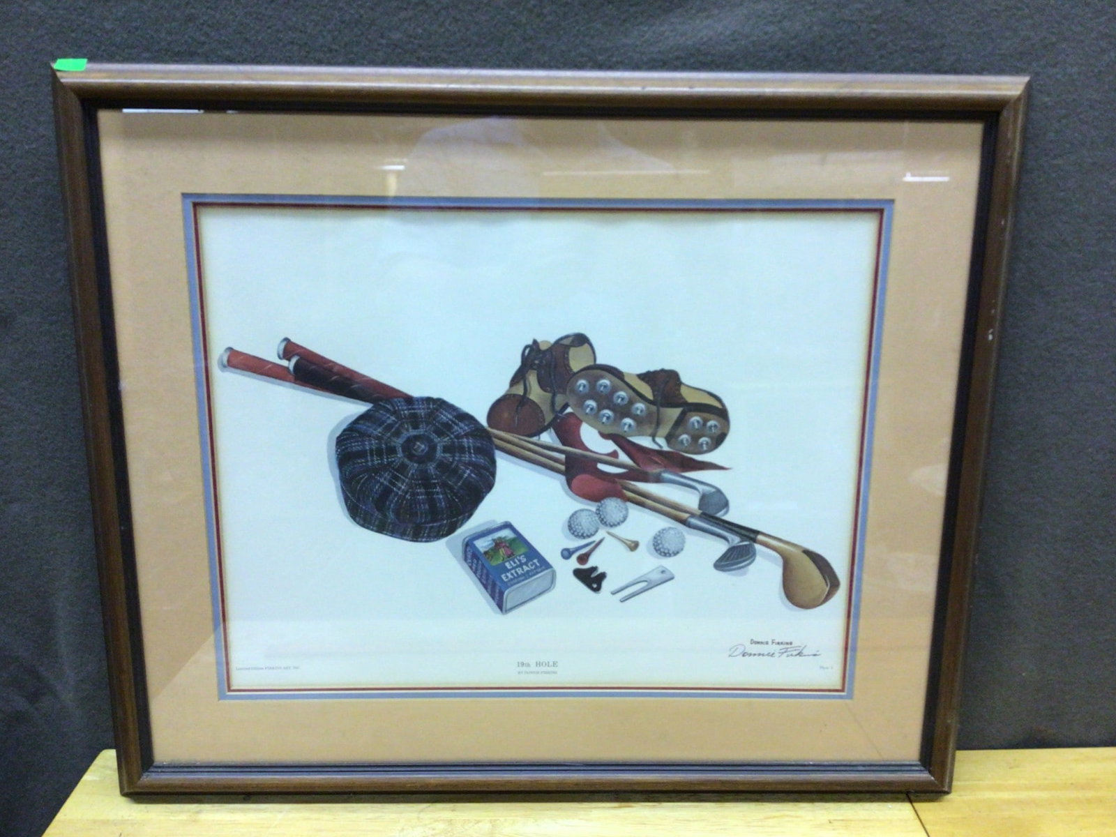 Framed Print Titled '19th Hole' by Artist Donnie Perkins: This is a framed print artwork titled '19th Hole,' created by artist Donnie Perkins. The print features a detailed depiction of golf-related items. It is signed by the artist on the lower right