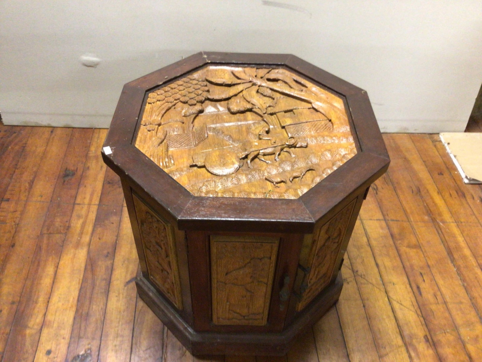 Octagonal Wooden Cabinet With Carved Top and Sides, 22 Inches Tall: Octagonal wooden cabinet with intricate carved scenes on the top and panels. The cabinet stands 22 inches tall and measures 23 1/2 inches from left to right (front to back). It includes hinged doors