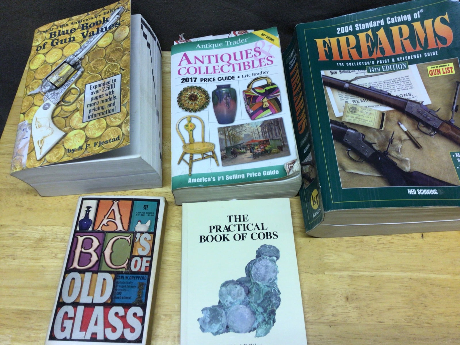 5 Reference Guides on Antiques, Firearms, Glass, and Coins: This lot features five reference guides: 'Antique Trader Antiques & Collectibles 2017 Price Guide,' '2004 Standard Catalog of Firearms,' 'Blue Book of Gun Values,' 'ABC's of Old Glass,' and 'The Pract