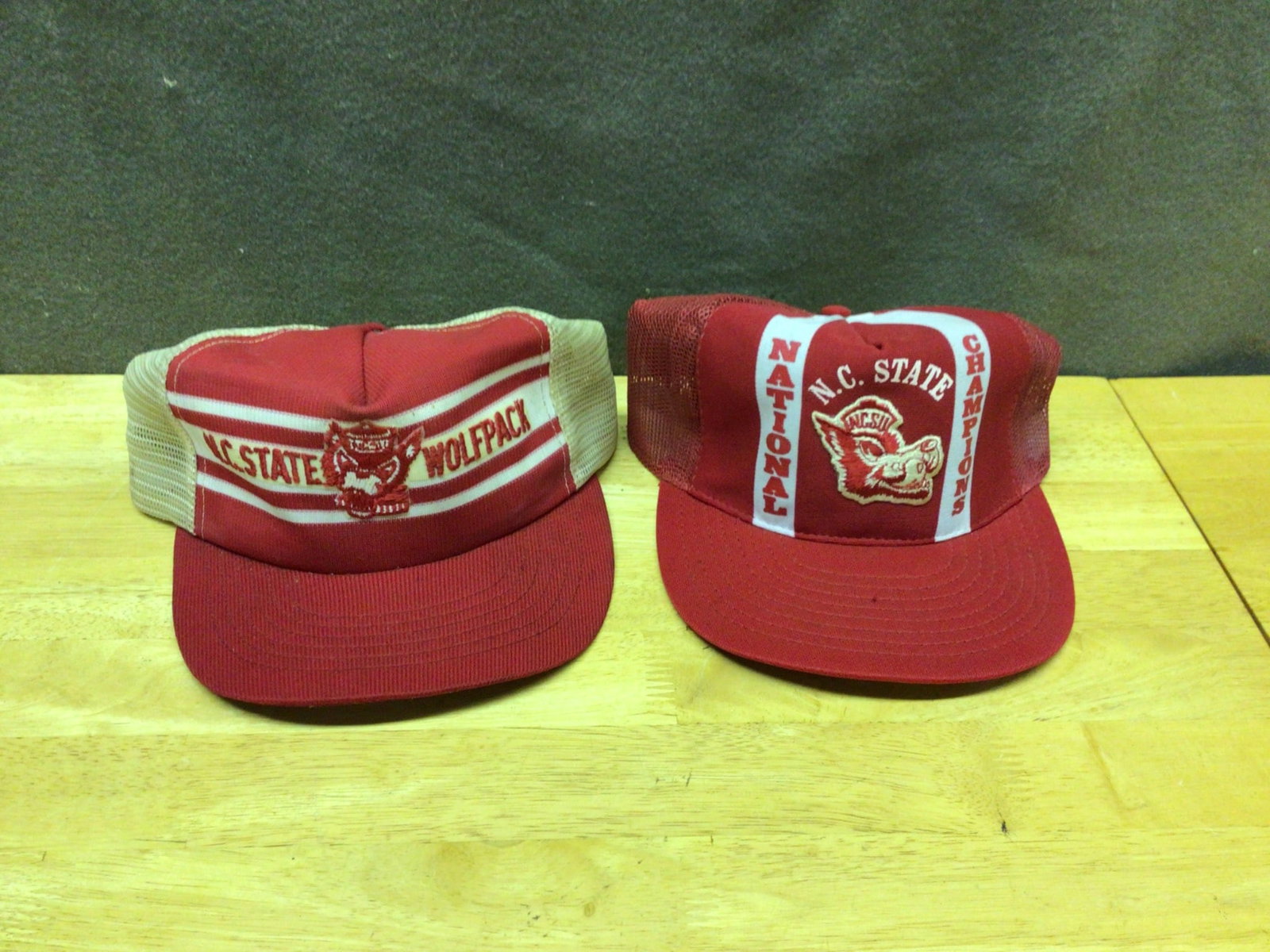 N.C. State Wolfpack Caps Featuring Team Graphics And National Champions Design: This lot includes two N.C State Wolfpack caps. The first cap features the Wolfpack logo and team name with mesh back and snapback closure. The second cap showcases the 'National Champions' text and