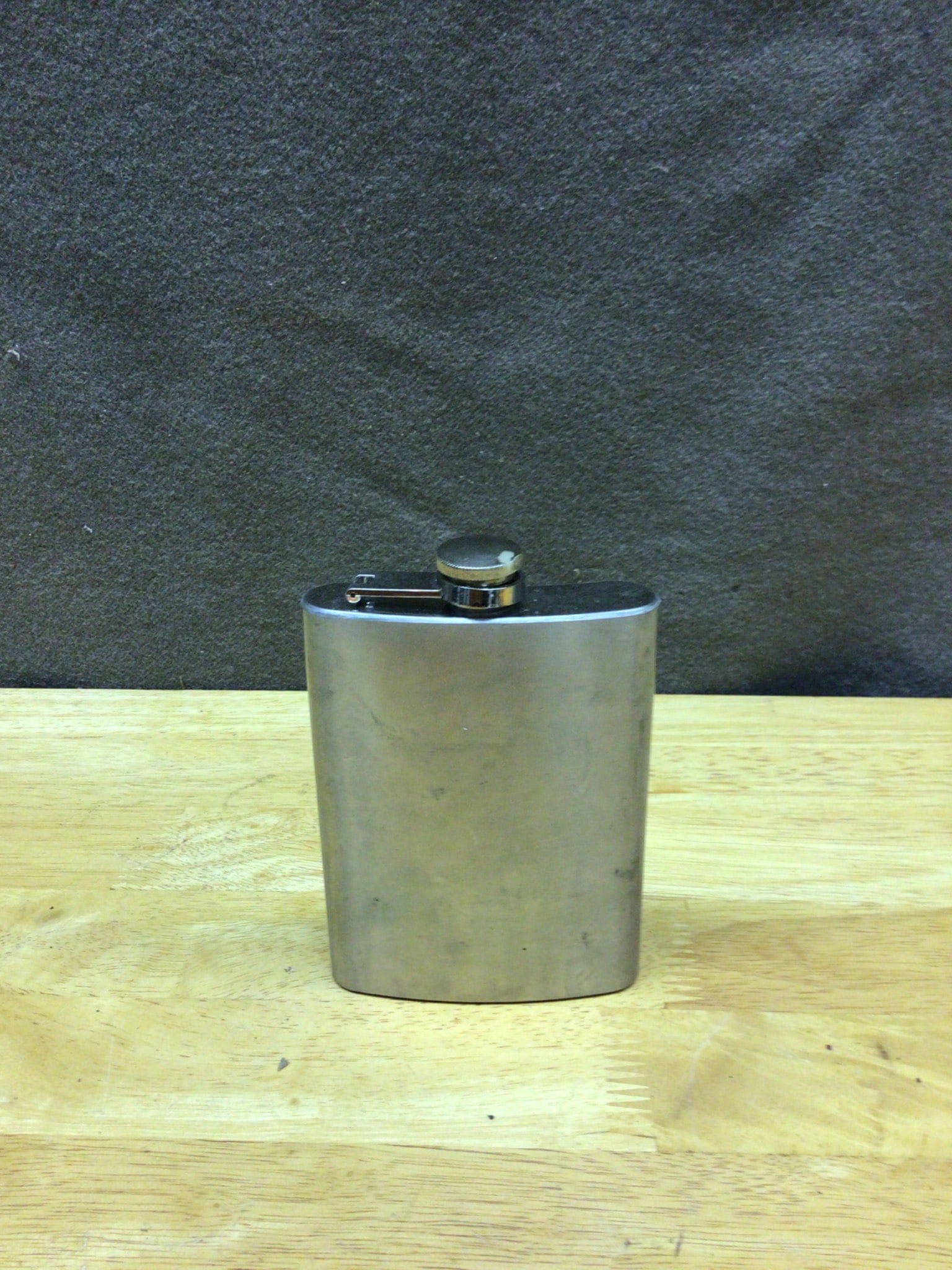 Stainless Steel 6 Oz Flask With Hinged Cap - Never Used: This lot includes a stainless steel 6 oz flask featuring a hinged cap for secure storage. The bottom is engraved with 'STAINLESS STEEL 6 OZ.' It has never been used, ensuring the interior is clean