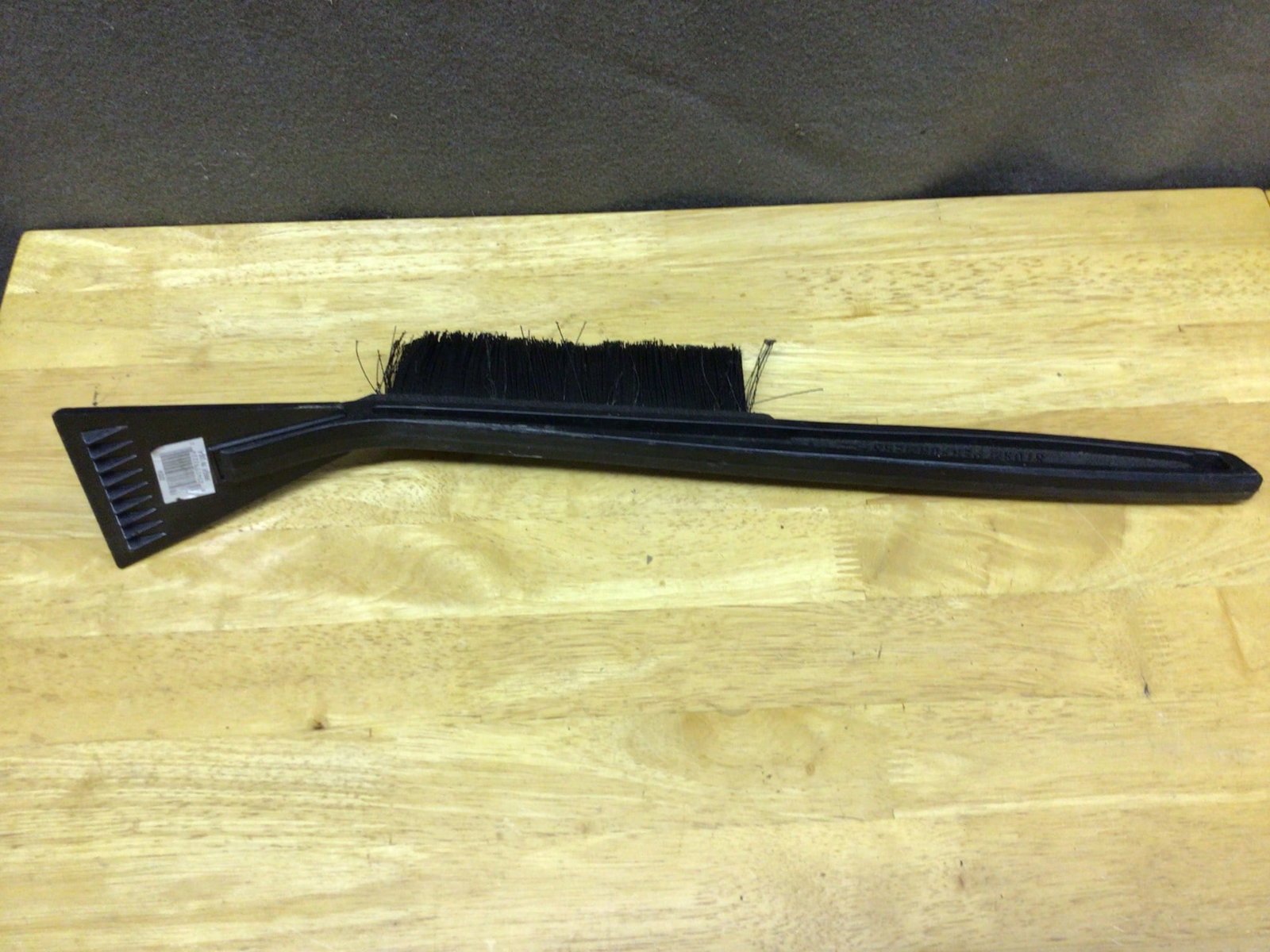 Plastic Handheld Brush and Scraper with Brand Inscription: A handheld plastic brush and scraper with an approximate length of 12 inches. Features a brush for cleaning tasks and a built-in scraper. The handle is embossed with the text 'Sloan Mfg Bakers.' This