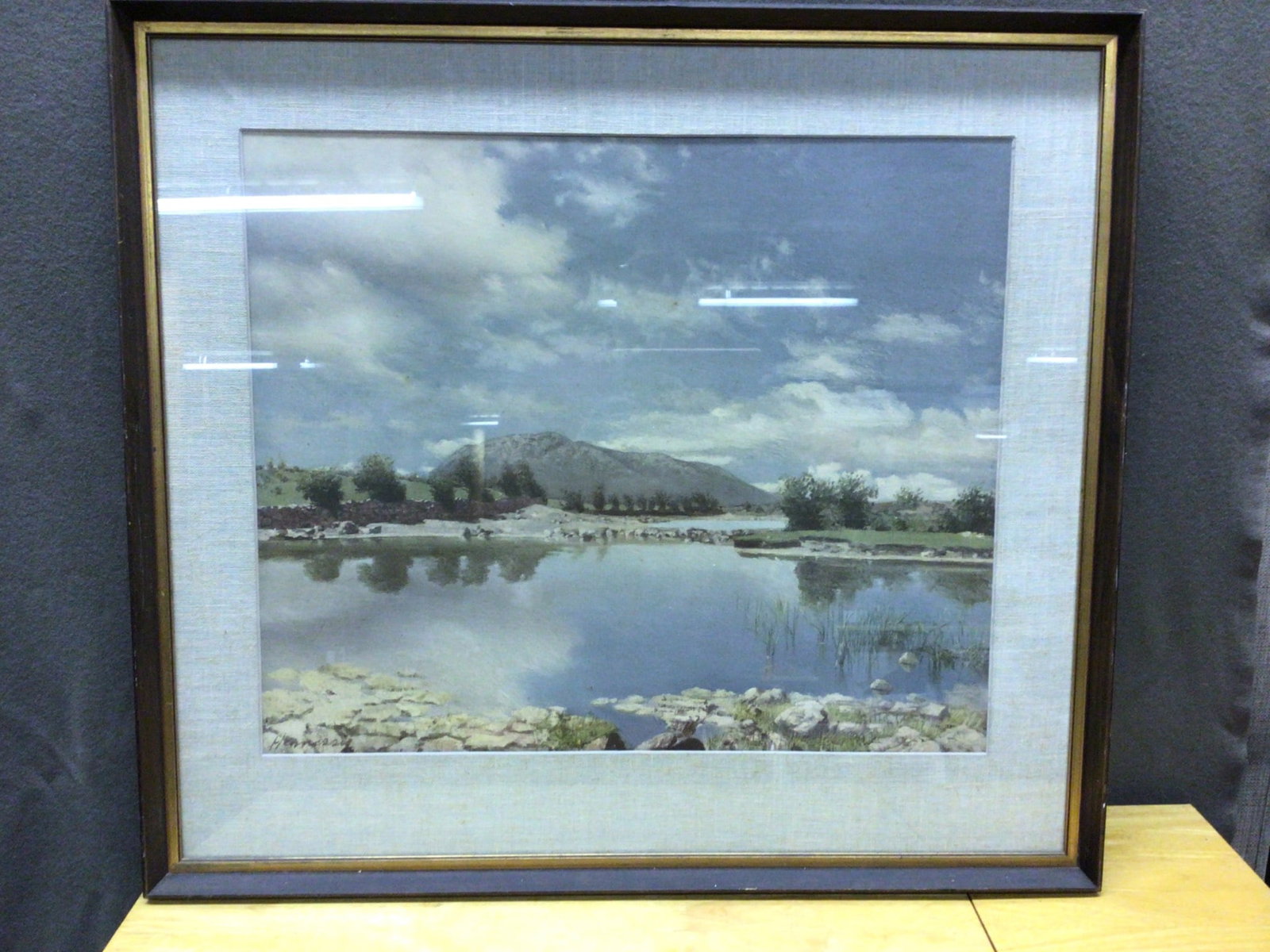 Framed Landscape Painting Depicting Mountain Scene With Signature: This framed landscape painting features a serene mountain and lake scene. The signature in the bottom left corner appears to read 'Hennington' (unverified). The approximate dimensions of the entire