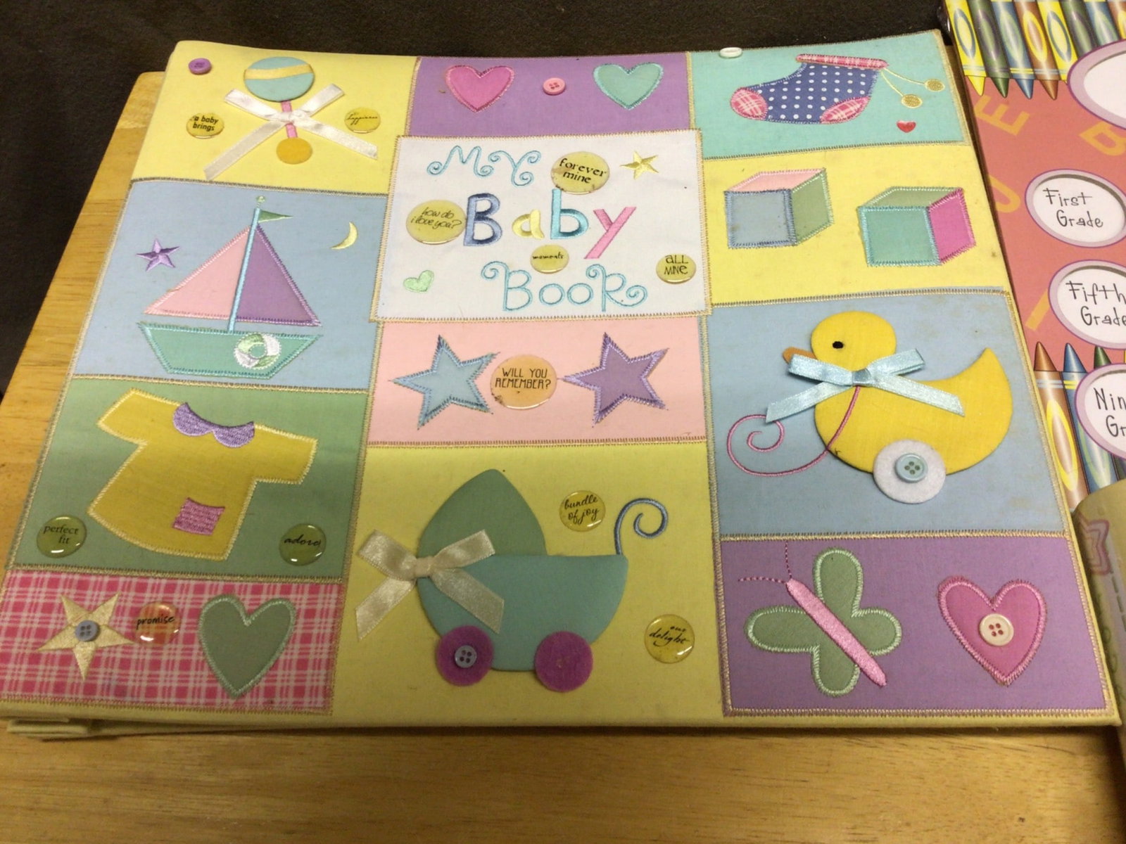 Baby Memory Book and Milestone Keepsake Set: A baby memory book featuring colorful covers with applique and ribbon accents, photo pages, and sleeves for documentation. Includes two additional frames: one for tracking yearly school photos