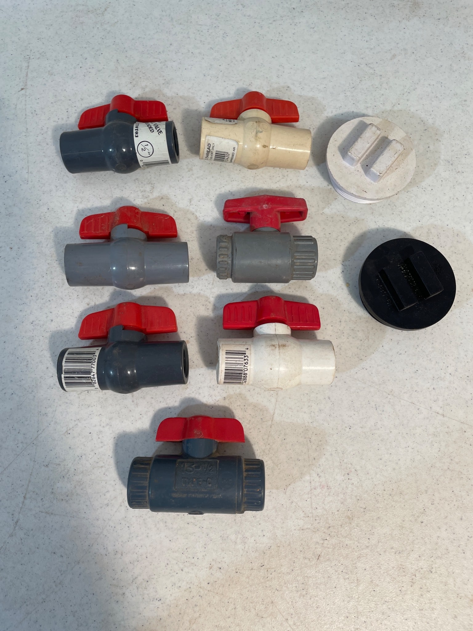 PVC Ball Valves and Plumbing End Caps: This lot includes seven PVC ball valves and two plumbing end caps. The ball valves feature red twist handles and are made of gray and white PVC material. The end caps appear to be made of PVC or