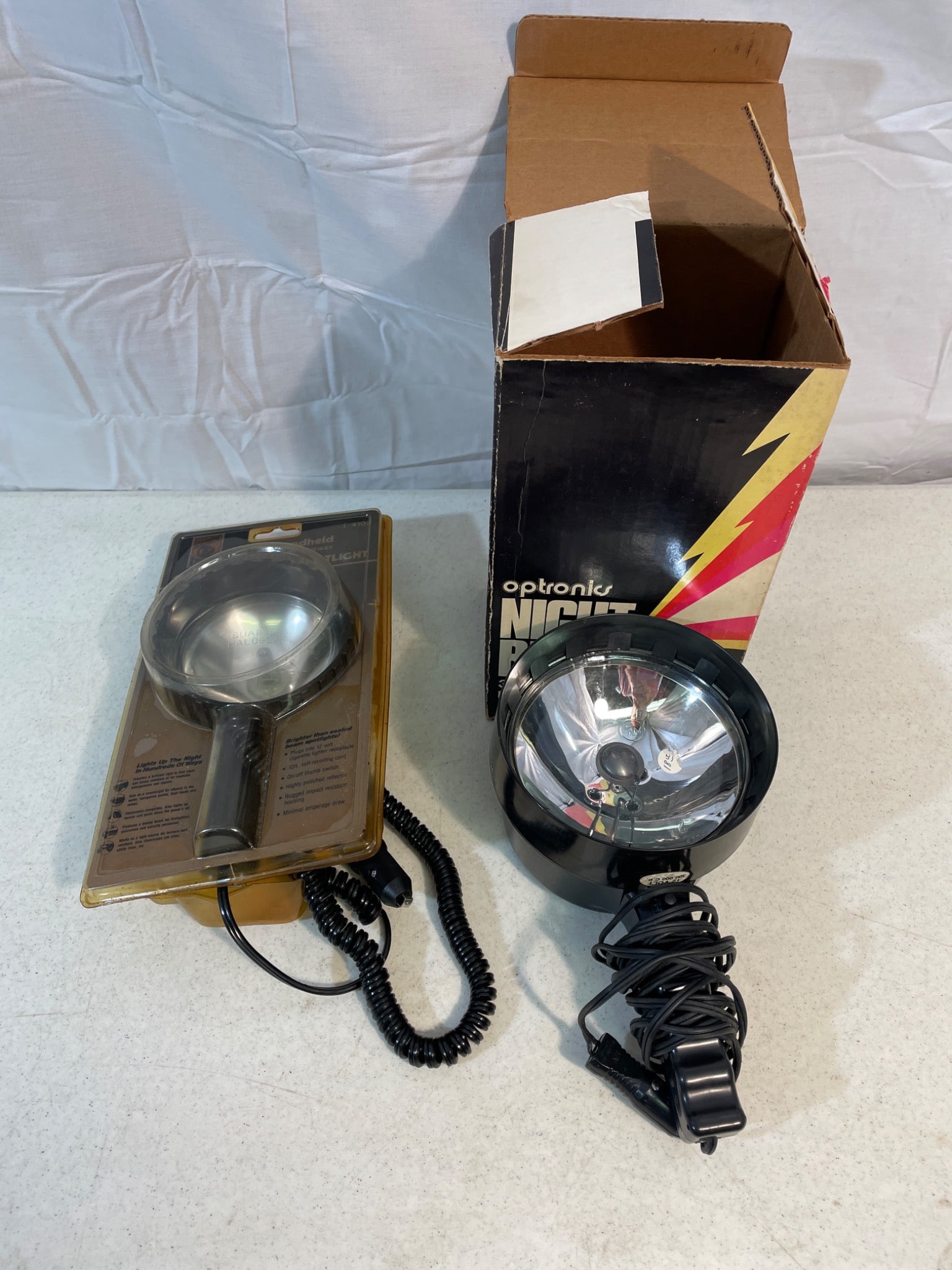 2 Handheld Spotlights, Optronics Night Blaster and Blazer L-4102: This lot includes two handheld 12-volt spotlights: the Optronics Night Blaster (300,000 candlepower, original box) and the Blazer L-4102 Quartz-Halogen Spotlight (100,000 candlepower, sealed in