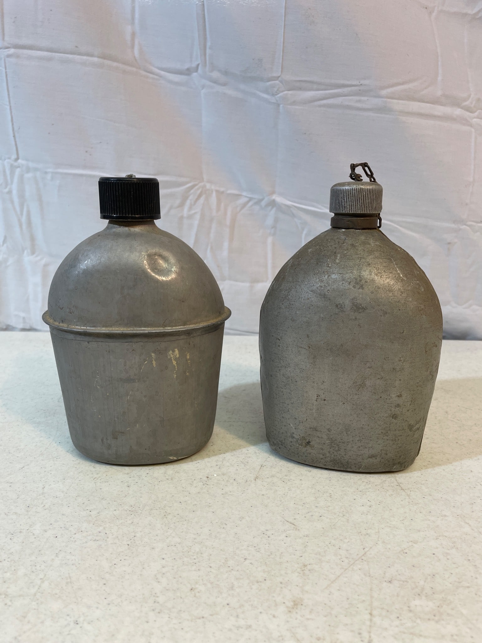 U.S. Military Metal Canteens, 1918 Marked, with Caps and Chains: Two U.S. military metal canteens. One is marked 'U.S. L.F.&C. 1918,' indicating production by Landers, Frary & Clark in 1918. Both feature attached screw-on caps with chain retainers and exhibit