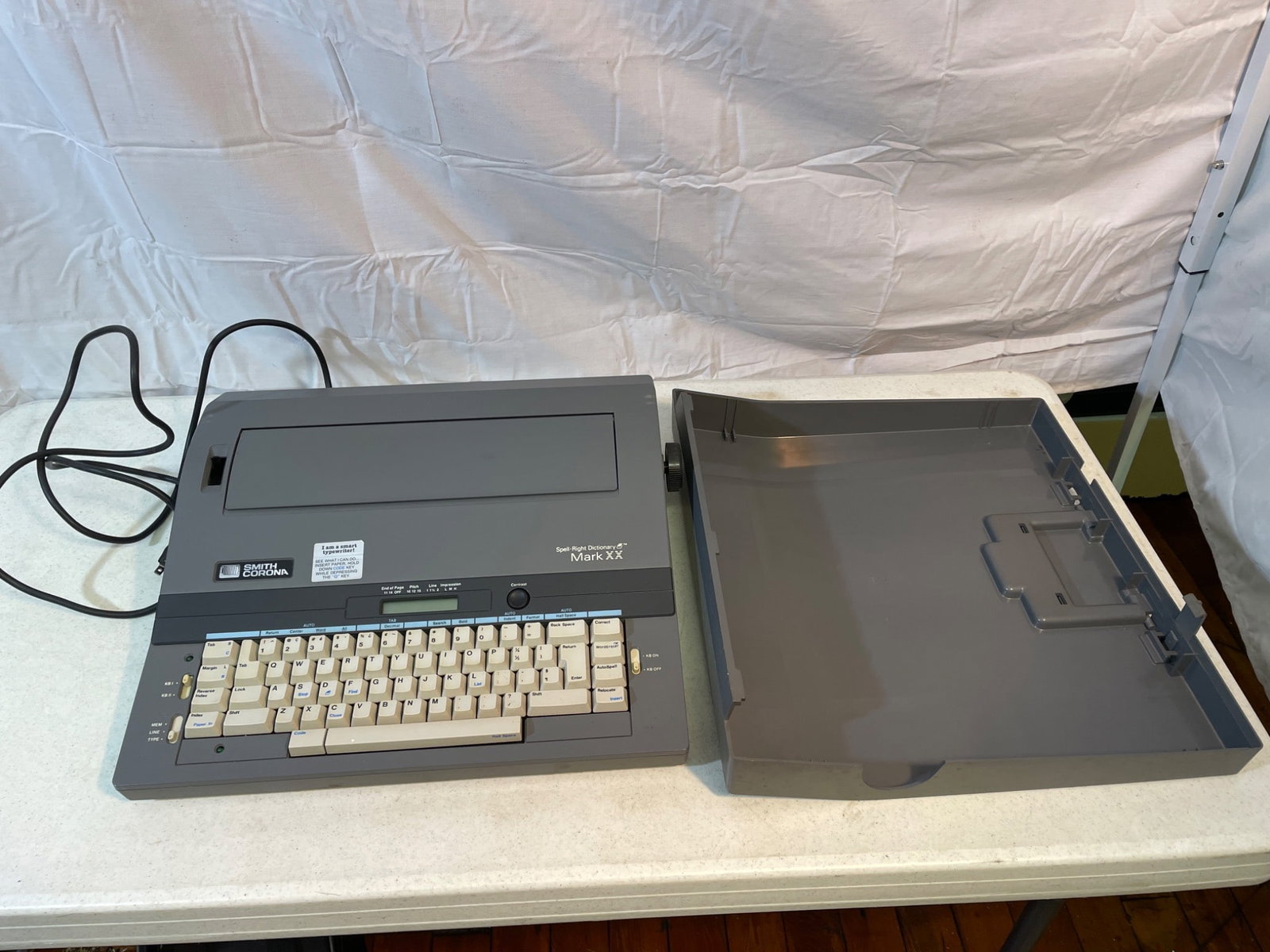 Smith Corona Electronic Typewriter Model Mark XII, Powers On: Smith Corona electronic typewriter, model Mark XII. Unit powers on as noted. Includes housing lid and power cord. Features an LCD display and QWERTY keyboard. Internal ribbon mechanism intact and