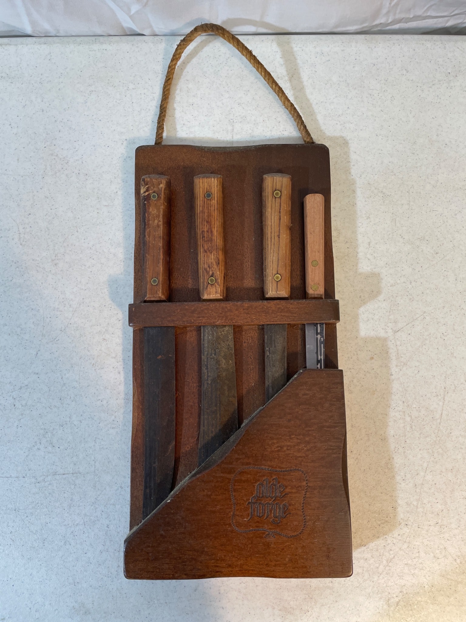 Four 'Olde Forge' Knives with Wooden Block Holder: Four knives labeled 'Olde Forge,' accompanied by a wooden storage block engraved with the brand name. Each knife features a wooden handle and various blade lengths and shapes. The condition shows