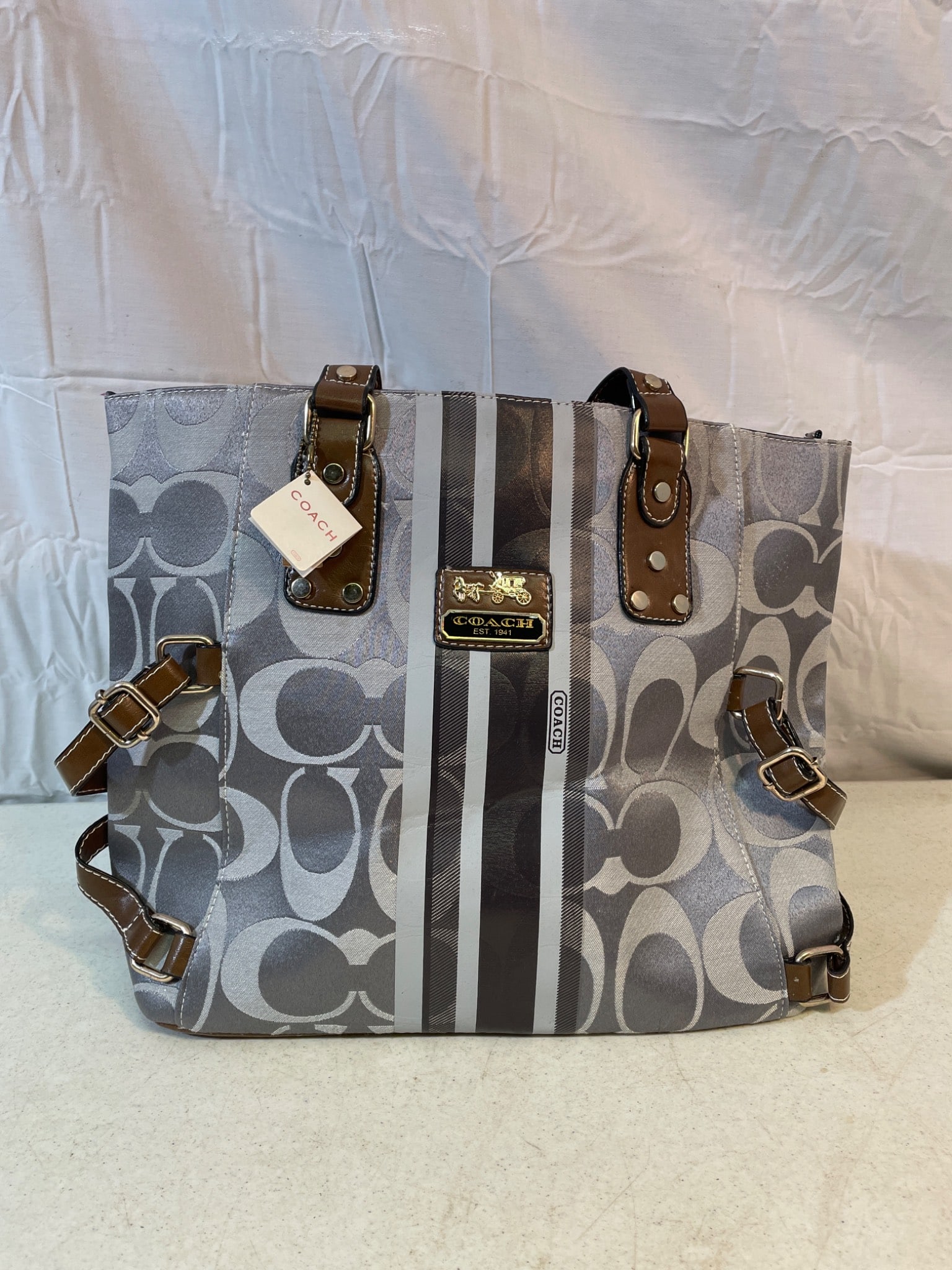 Coach Signature Stripe Coated Canvas Tote with Leather Trim: Coach signature stripe coated canvas tote with leather trim and brass hardware. Features an open top with snap closure, fabric-lined interior with zippered and slip pockets, and adjustable side
