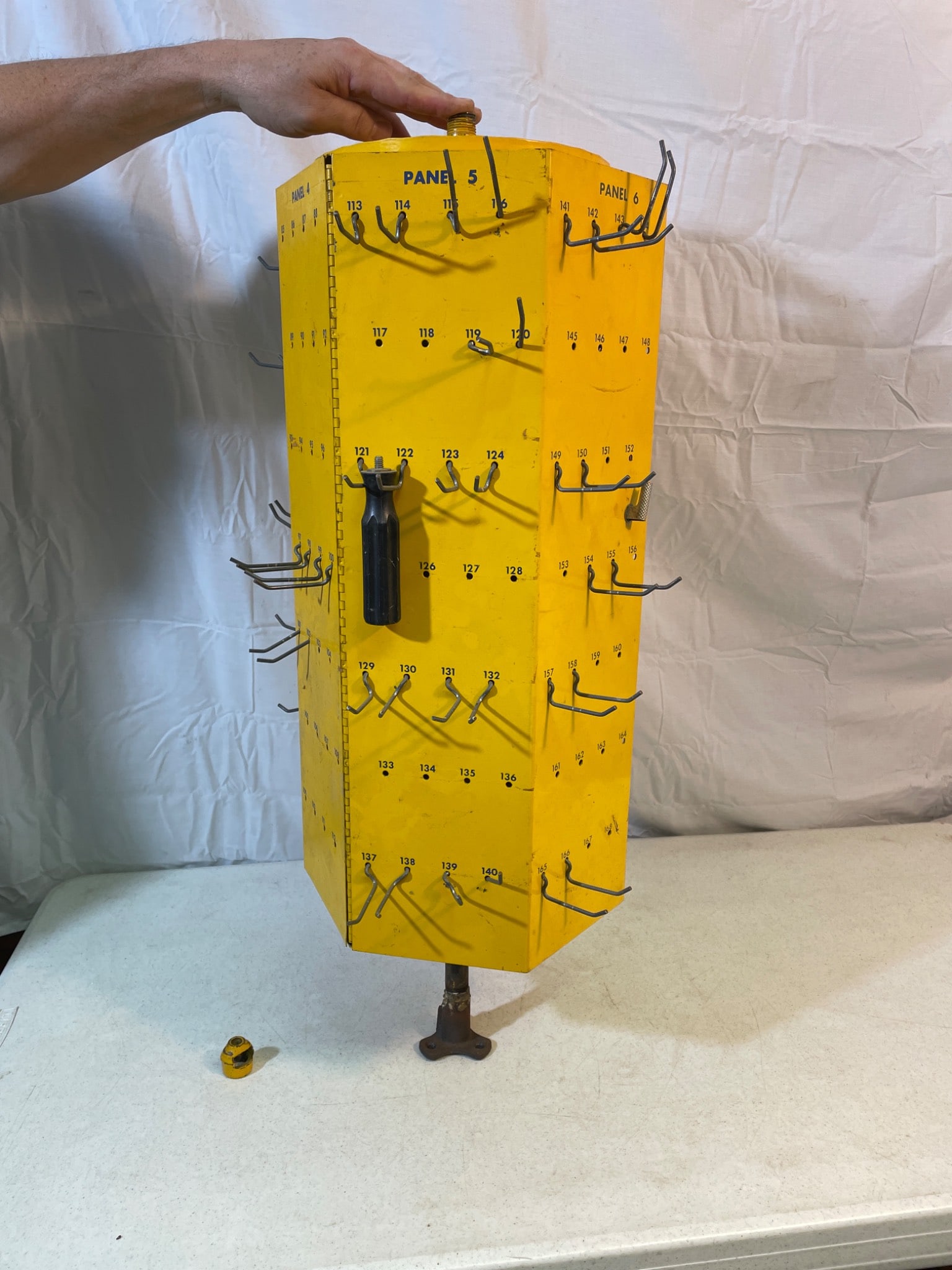 Rotating Metal Storage Bin with Hooks and Panels: A rotating metal storage bin with yellow-painted panels. It features four vertical panels with multiple hooks for tool or accessory organization. The central column is supported by a stand. The unit