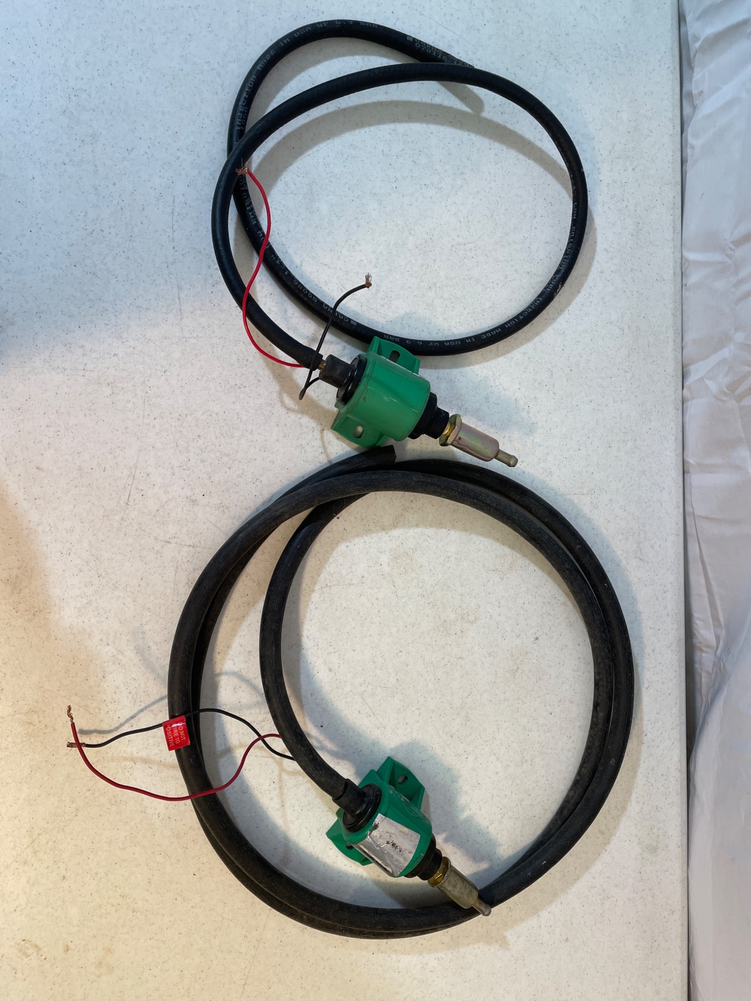 Two GPI Electronic Fuel Meter Assemblies With Hoses: This lot includes two GPI electronic fuel meter assemblies fitted with hoses. The green casing houses the meter mechanism, and the units are marked with directional flow indicators. The hoses appear