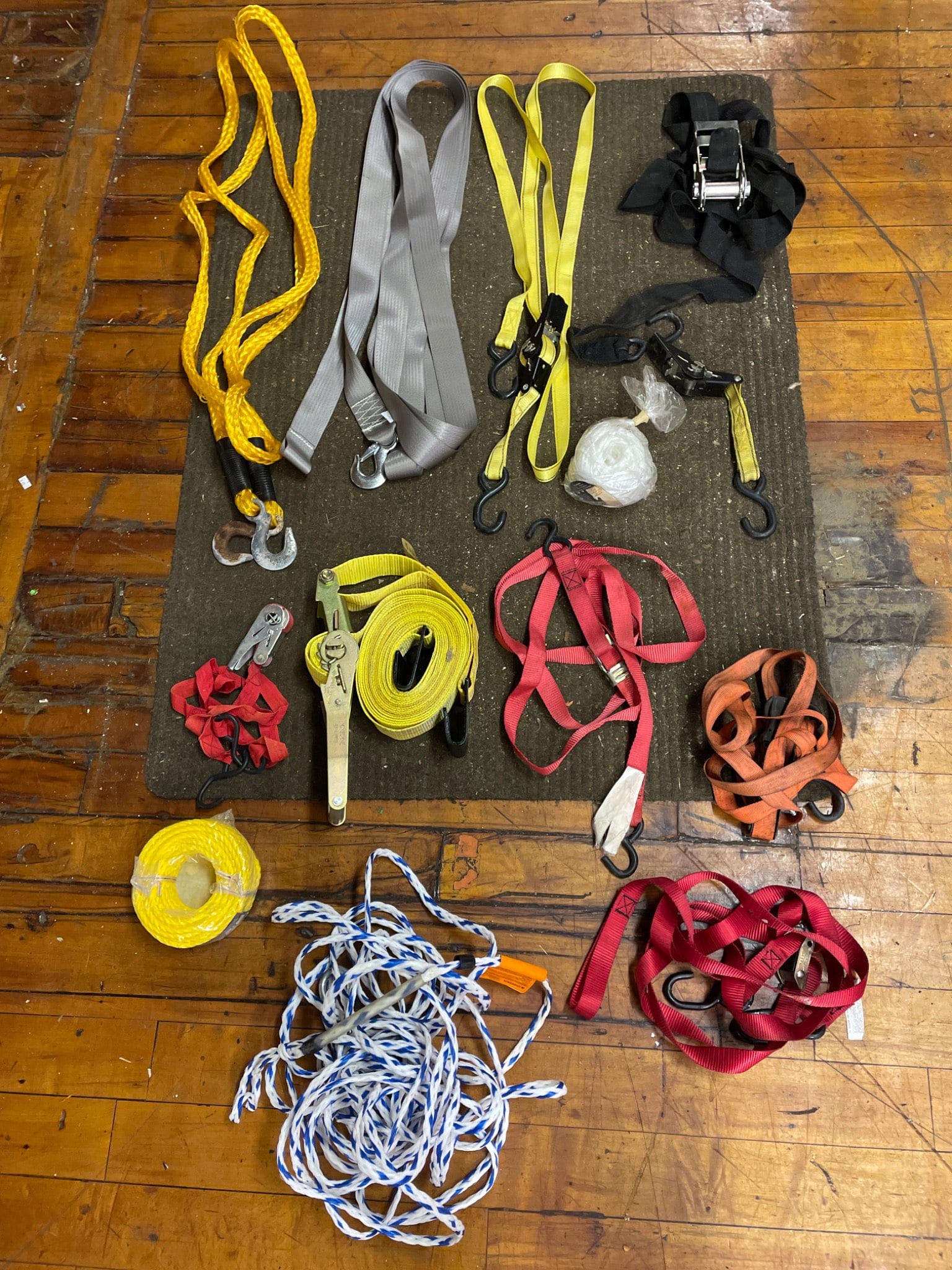 Load-Bearing Straps, Tie-Downs, and Ropes: Various load-bearing straps, tie-downs, ratchet straps, and ropes. Items are in mixed colors such as red, yellow, grey, and black. Includes hooks and ratchets for securing loads. Inspect for