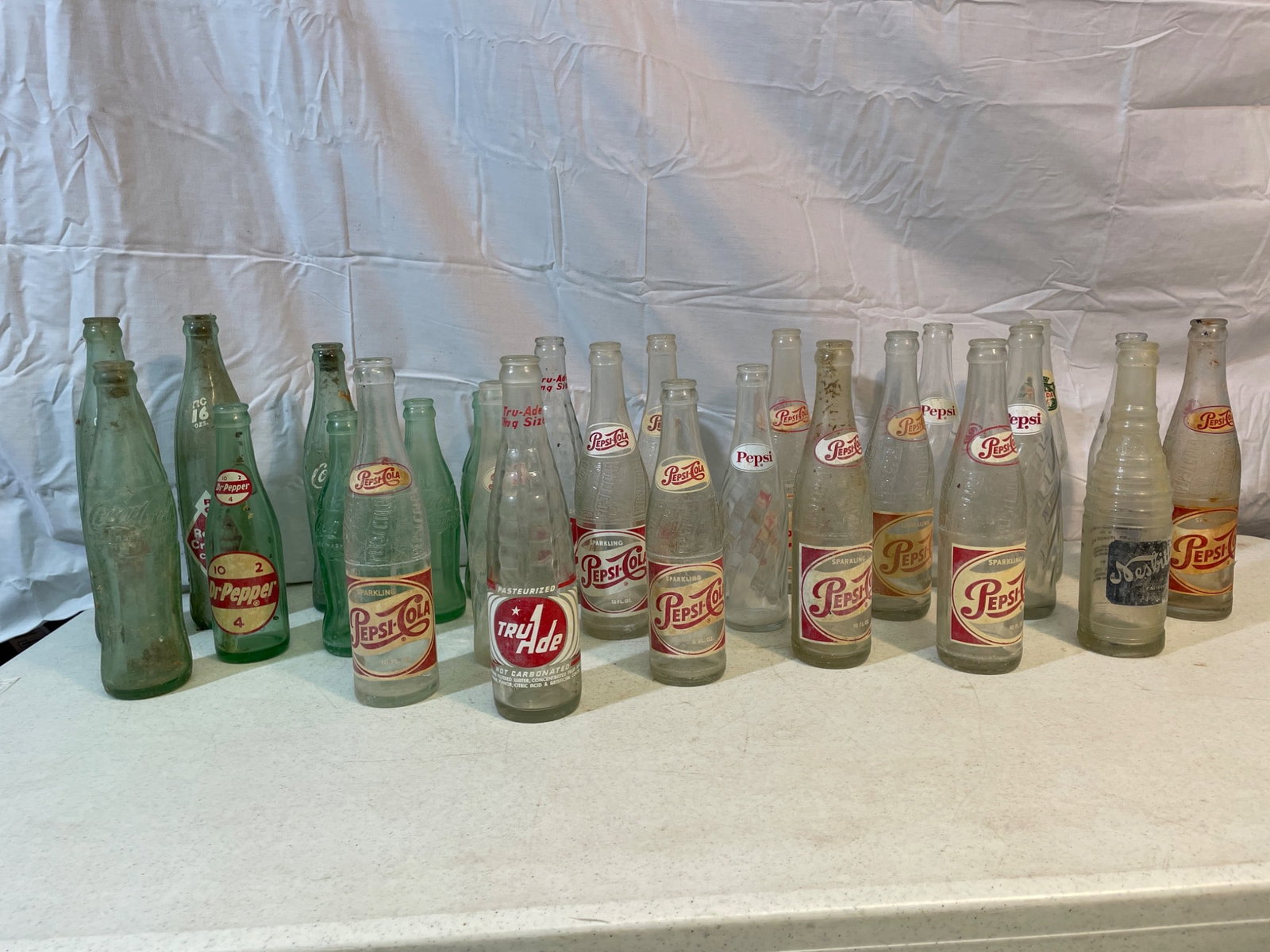 Vintage Soda Bottles Including Pepsi, Royal Crown, and Tru-Ade: This lot includes a collection of mixed vintage soda bottles from brands such as Pepsi, Royal Crown (RC) Cola, Dr. Pepper, and Tru-Ade. The collection features various designs, including embossed and 