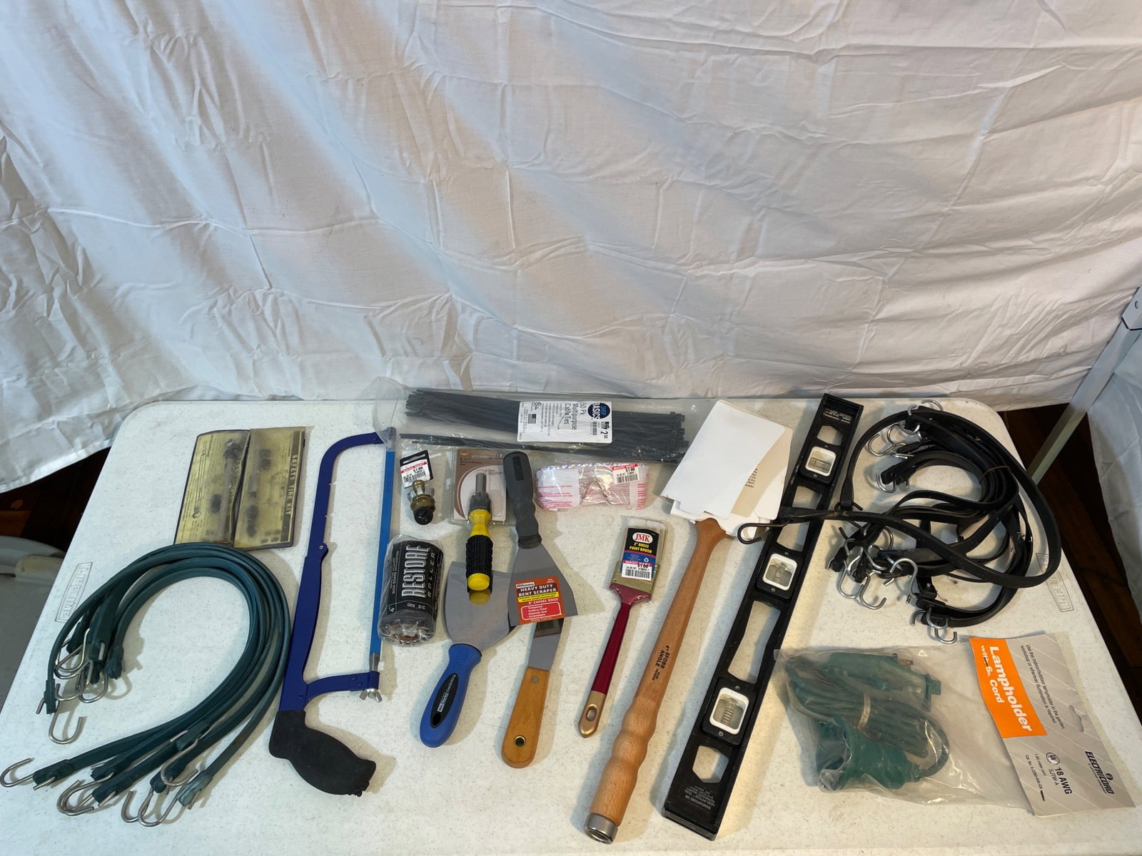 Hand Tools and Accessories Including Brushes, Saw, and Bungee Cords: Tools such as bungee cords, paint brushes, a hacksaw, measuring tape, a level, zip ties, electrical cord with adapter, screwdrivers, putty knives, and other items. Tools are a mix of materials and bra