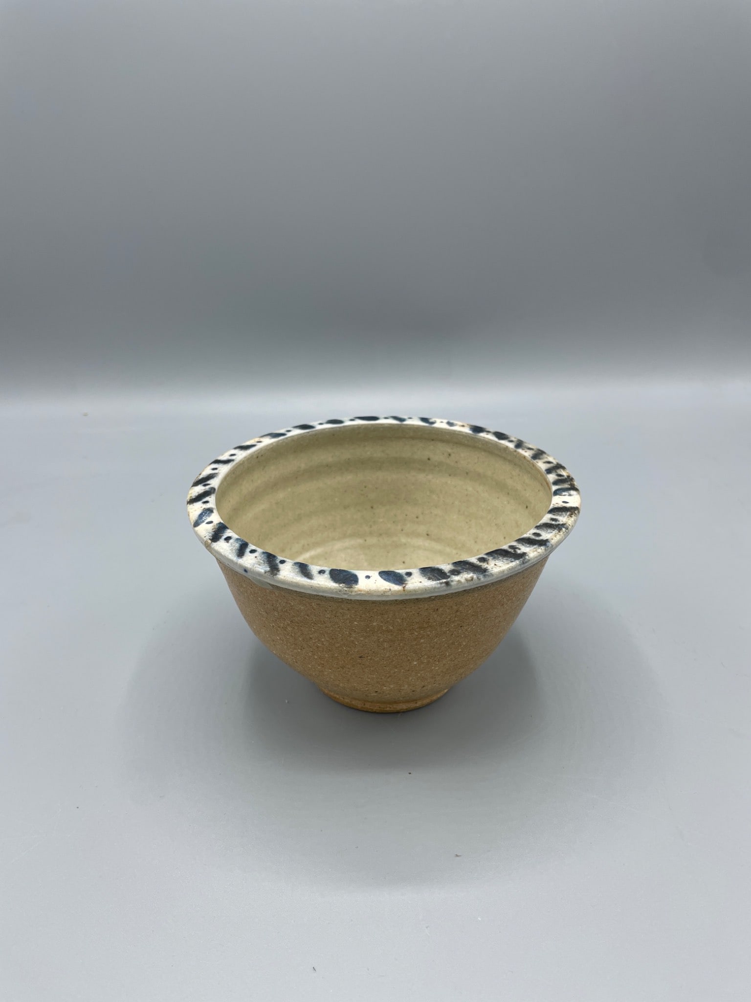 Stoneware Bowl With Blue Speckled Rim, Floral Interior Design: Handcrafted stoneware bowl featuring a blue speckled rim and a floral pattern on the interior. The bowl appears to have a natural clay finish with glazed accents. Measures approximately 4 inches in