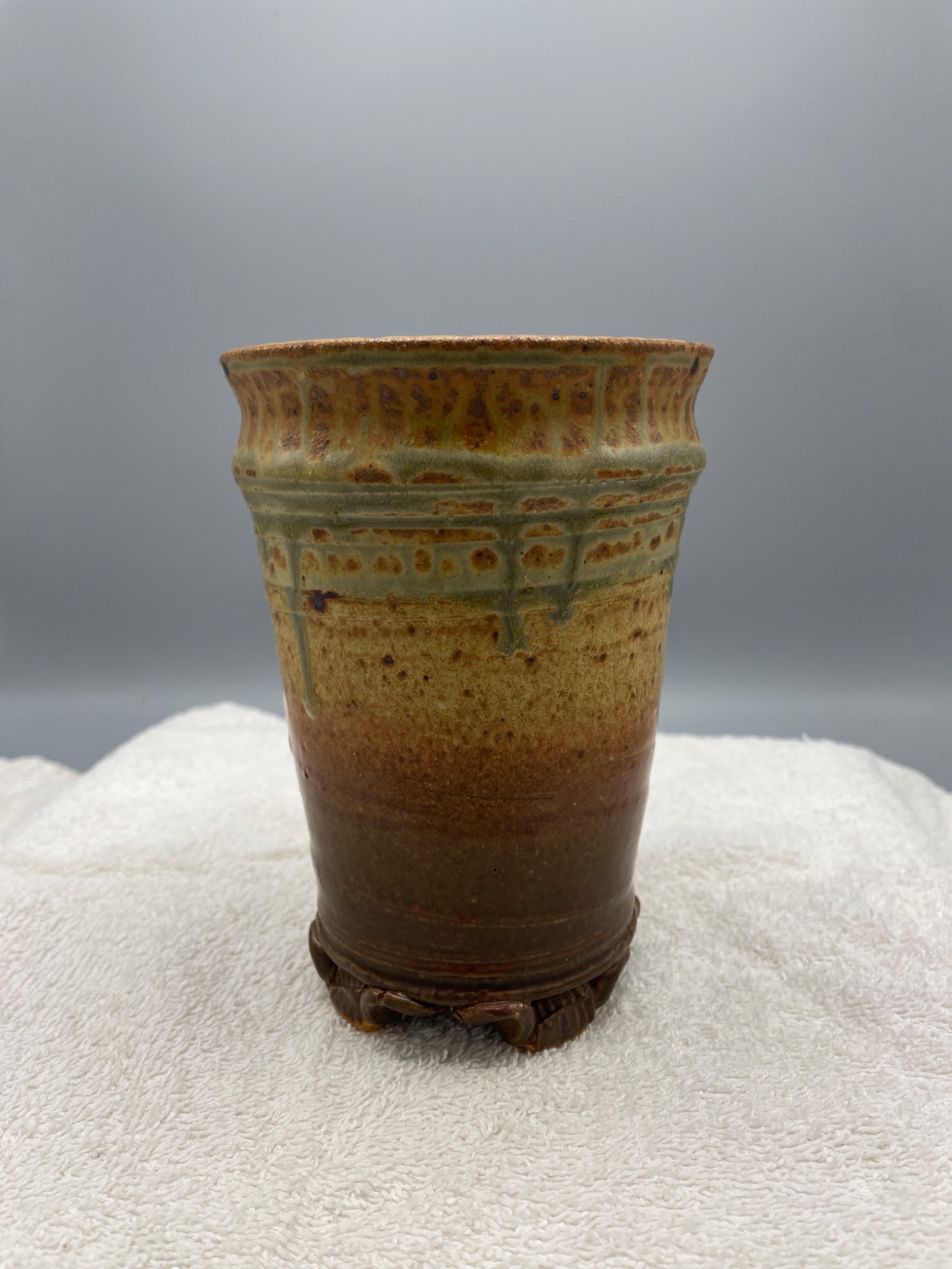 Stoneware Cup with Glazed Finish and Stamped Base: A stoneware cup with a multicolored glazed finish, standing approximately 4.5 inches tall. The piece features decorative motifs and includes inscriptions on the base, possibly the artist's markings.