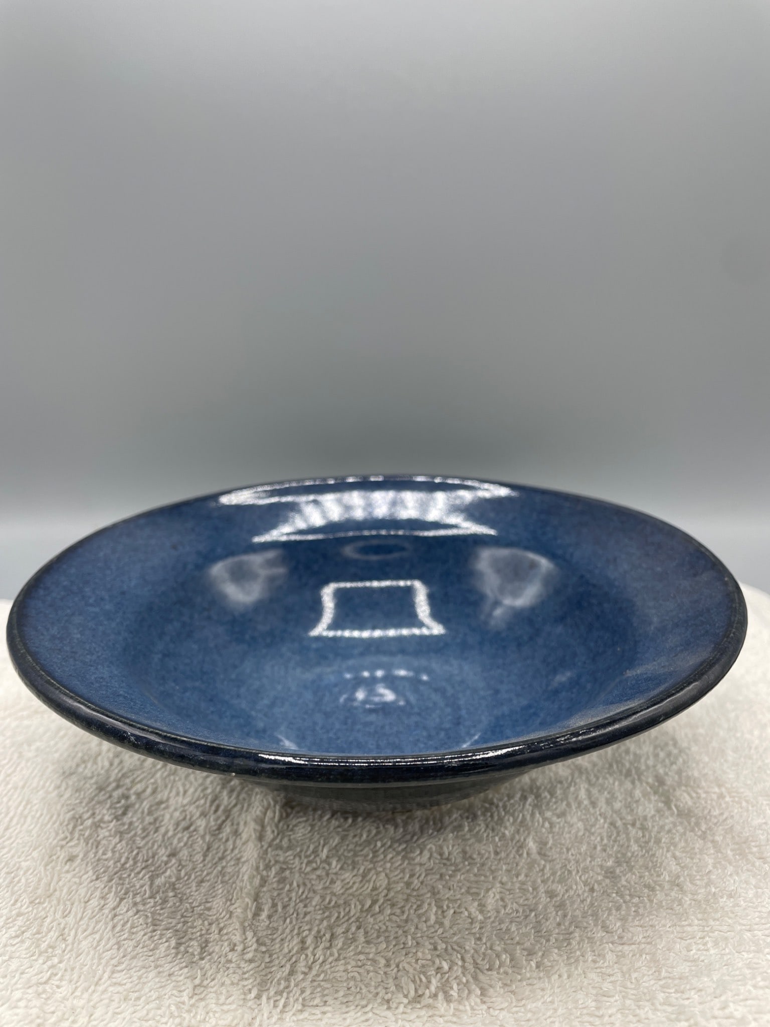 Blue Ceramic Bowl with Glazed Finish, Unknown Manufacturer: This is a blue ceramic bowl with a glazed finish and an unmarked base. It measures approximately 2 inches in height based on the accompanying ruler. The bowl appears to be hand-crafted, as indicated