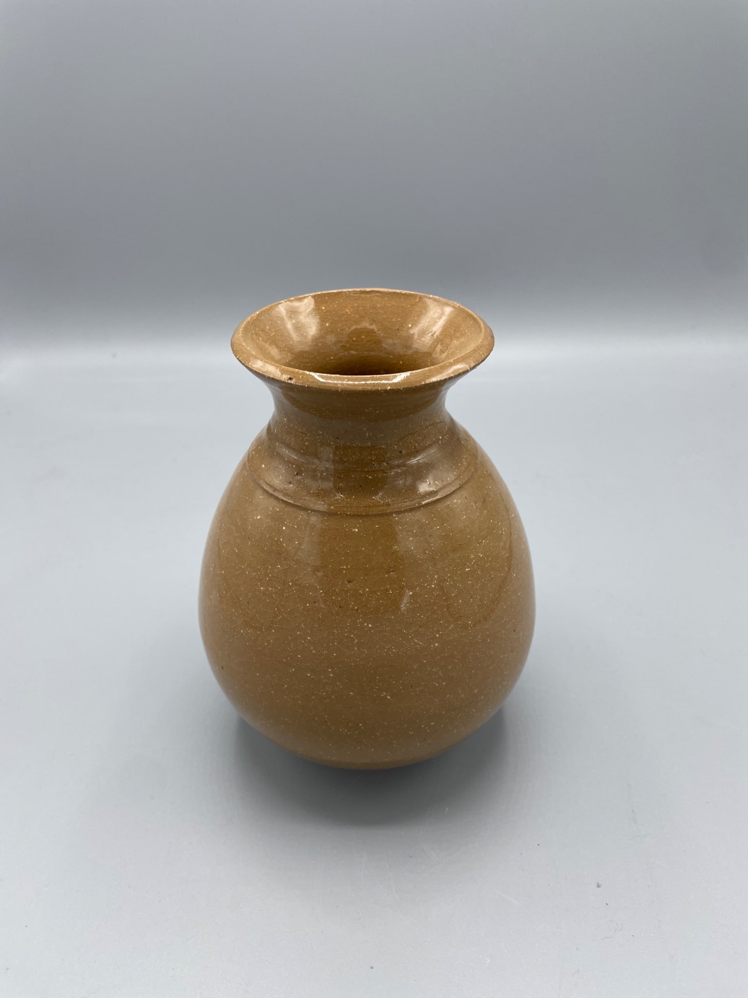 Brown Ceramic Vessel With Flared Rim and Rounded Body: This is a small ceramic vessel with a flared rim and rounded body. The base features an unglazed ring with a possible maker's mark or symbol. The glossy brown finish has a speckled effect. The height