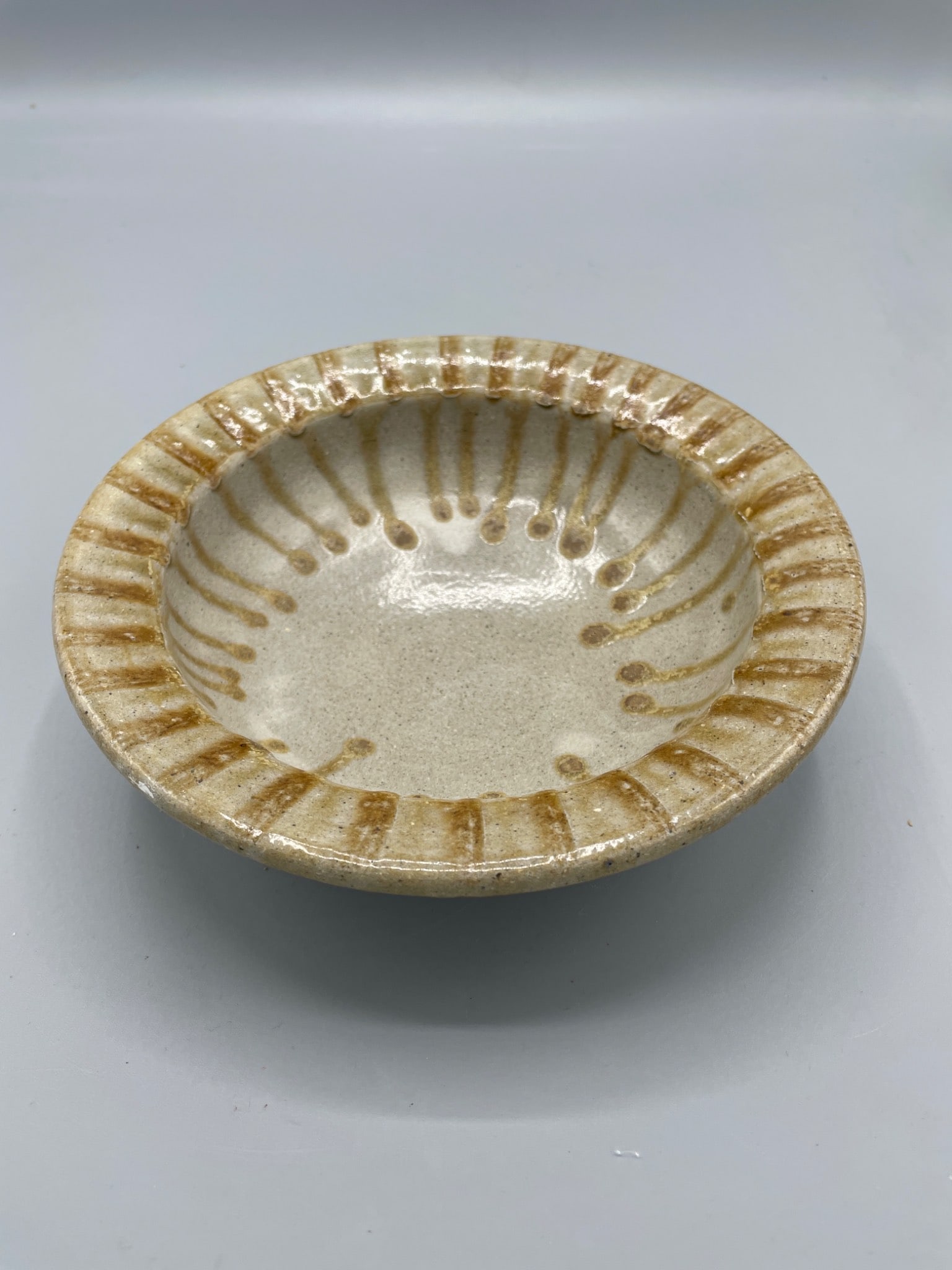Handcrafted Ceramic Bowl with Brown and Beige Glaze, Signed Base Mark 'D': This ceramic bowl features a beige glaze accented with brown drip detailing along the rim and interior. The base is signed with a 'D' mark, indicative of the artisan or manufacturer. It measures