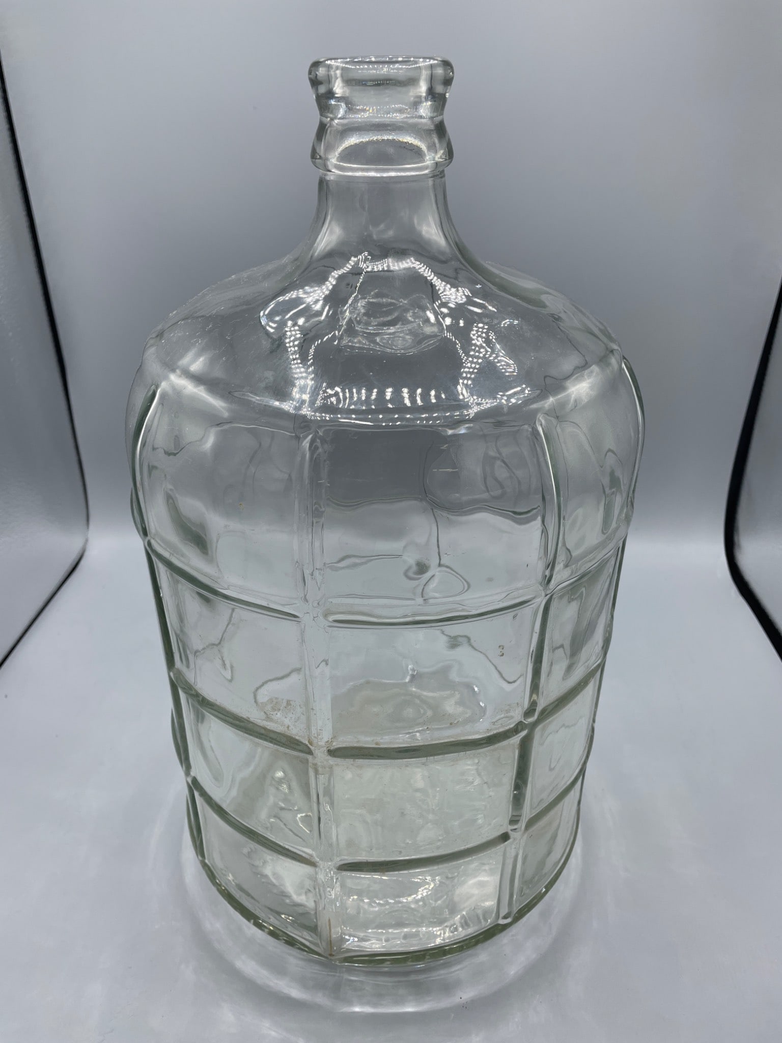 16-Inch Clear Glass Carboy with Embossed Base: A 16-inch clear glass carboy with a textured, embossed design on the base and a grid-like pattern on the surface. Suitable for liquid storage. Approximately 16 inches tall as shown in photo. Base