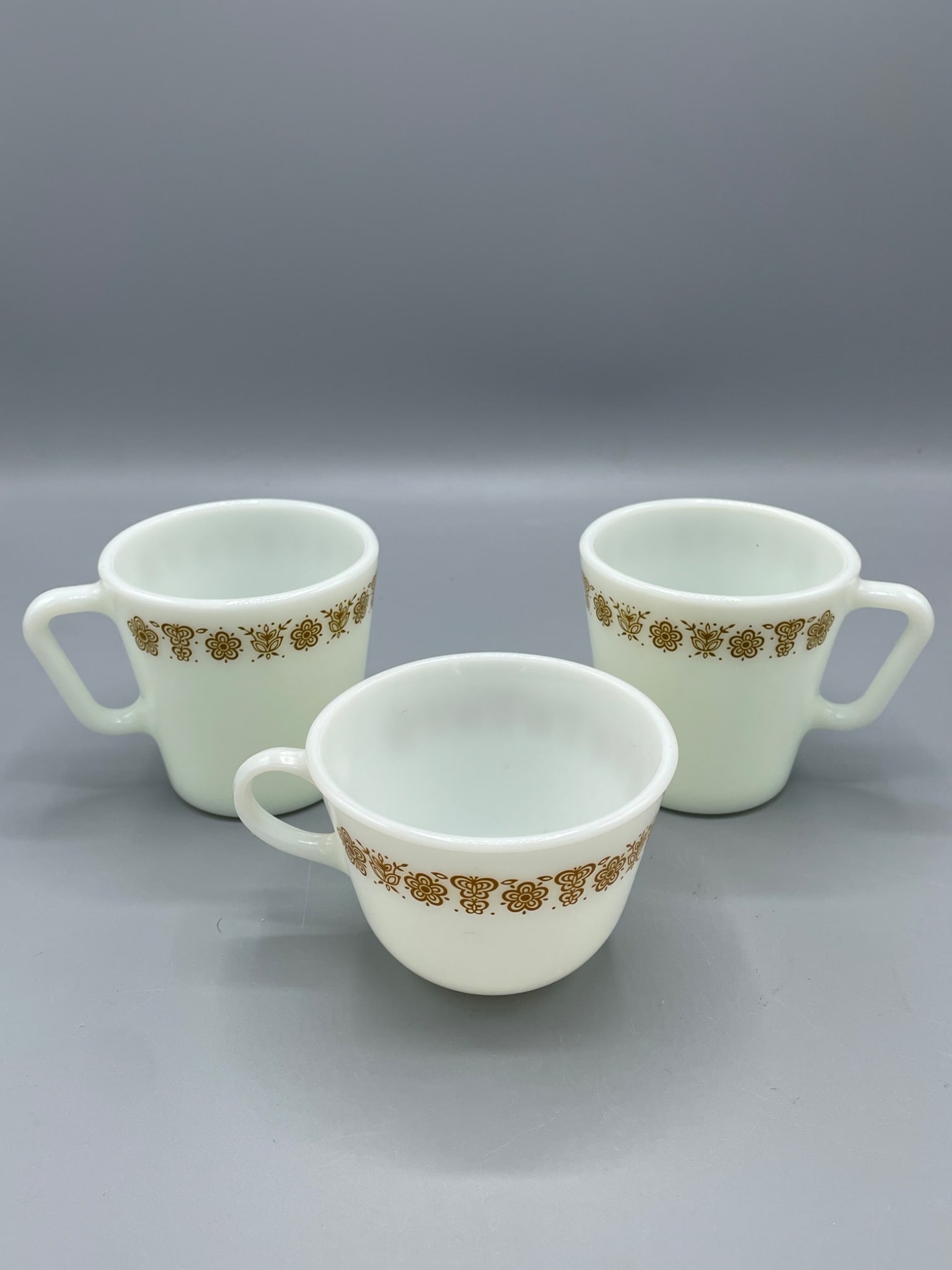 Three Pyrex USA Model No. 1410 and 702 Cups with Floral Design: This set includes three Pyrex cups, made in the USA. Two of the cups are marked as Model No. 1410, while the third is Model No. 702, as observed on the base of each cup. They are microwave-safe and fe
