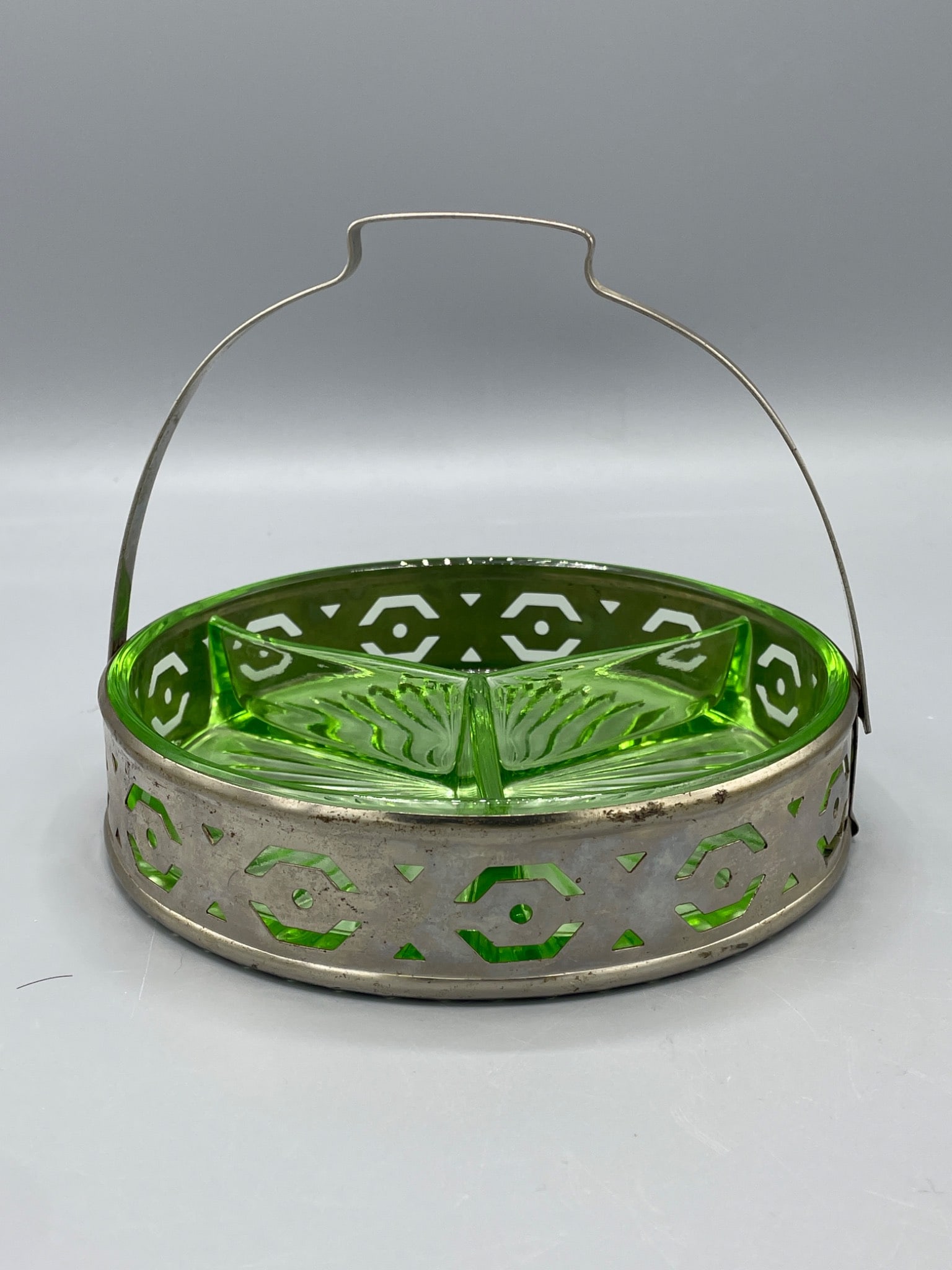 Divided Uranium Glass Dish with Metal Carrier: A divided uranium glass dish featuring a three-section design housed within a metal carrier with a geometric pattern. The dish fluoresces under UV light. Includes a decorative handle for easy