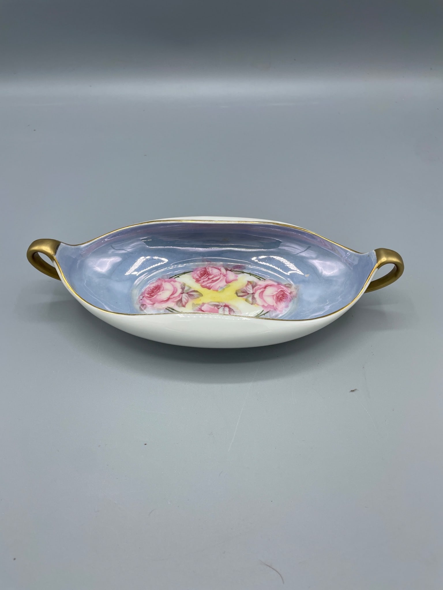 LR Bavaria Porcelain Dish with Floral Design and Gold Handles: This is a porcelain dish marked "LR Bavaria" on the bottom, indicating it was manufactured in Germany. The piece features a floral rose design on a light blue background with gold-painted handles. It