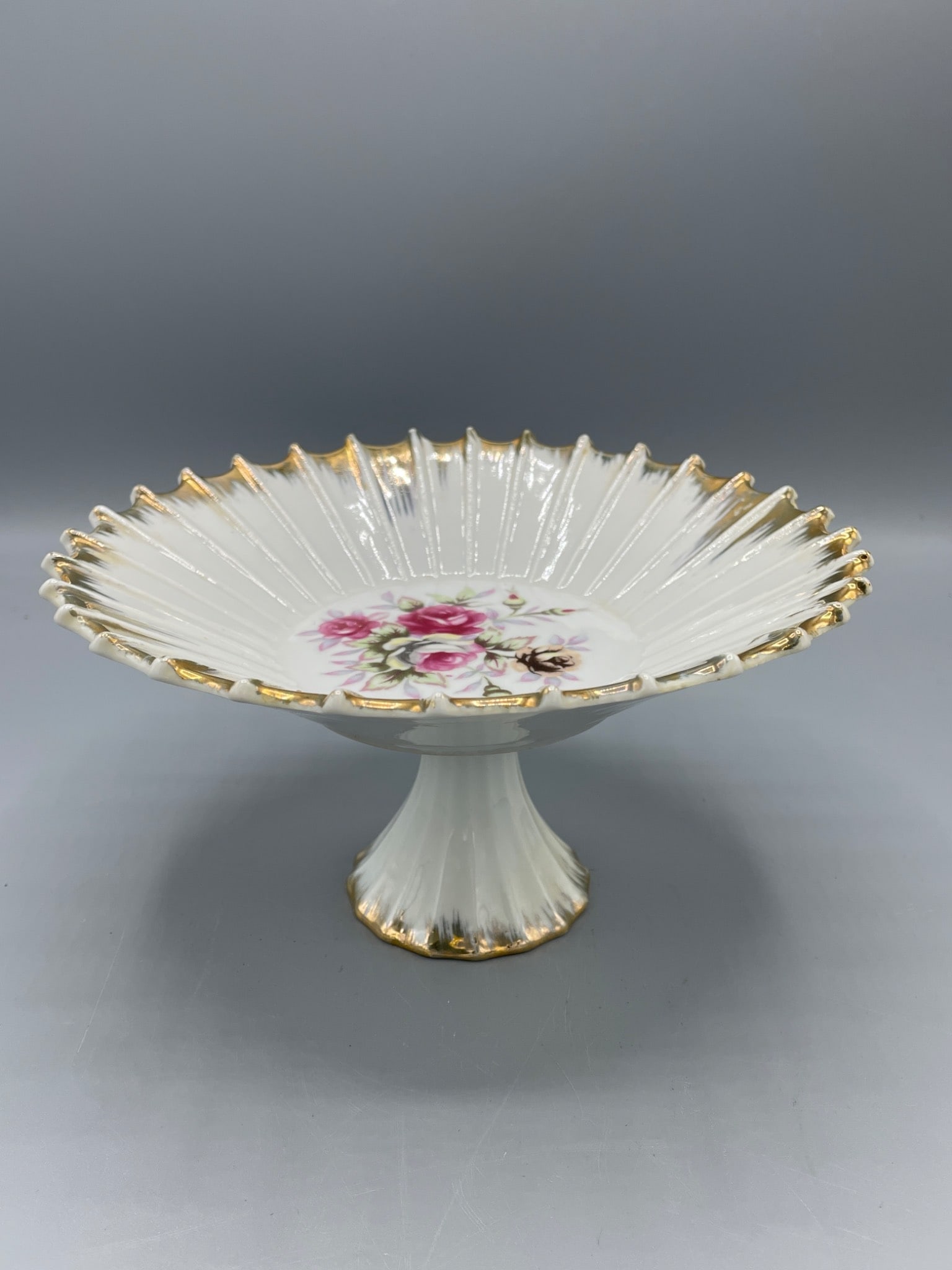 Porcelain Pedestal Cake Stand with Floral Design and Gold Trim, Model E-3012: This porcelain pedestal cake stand features a scalloped edge design with gold trim accents and a pink floral motif in the center. The underside of the stand is marked 'E-3012'. The item shows signs