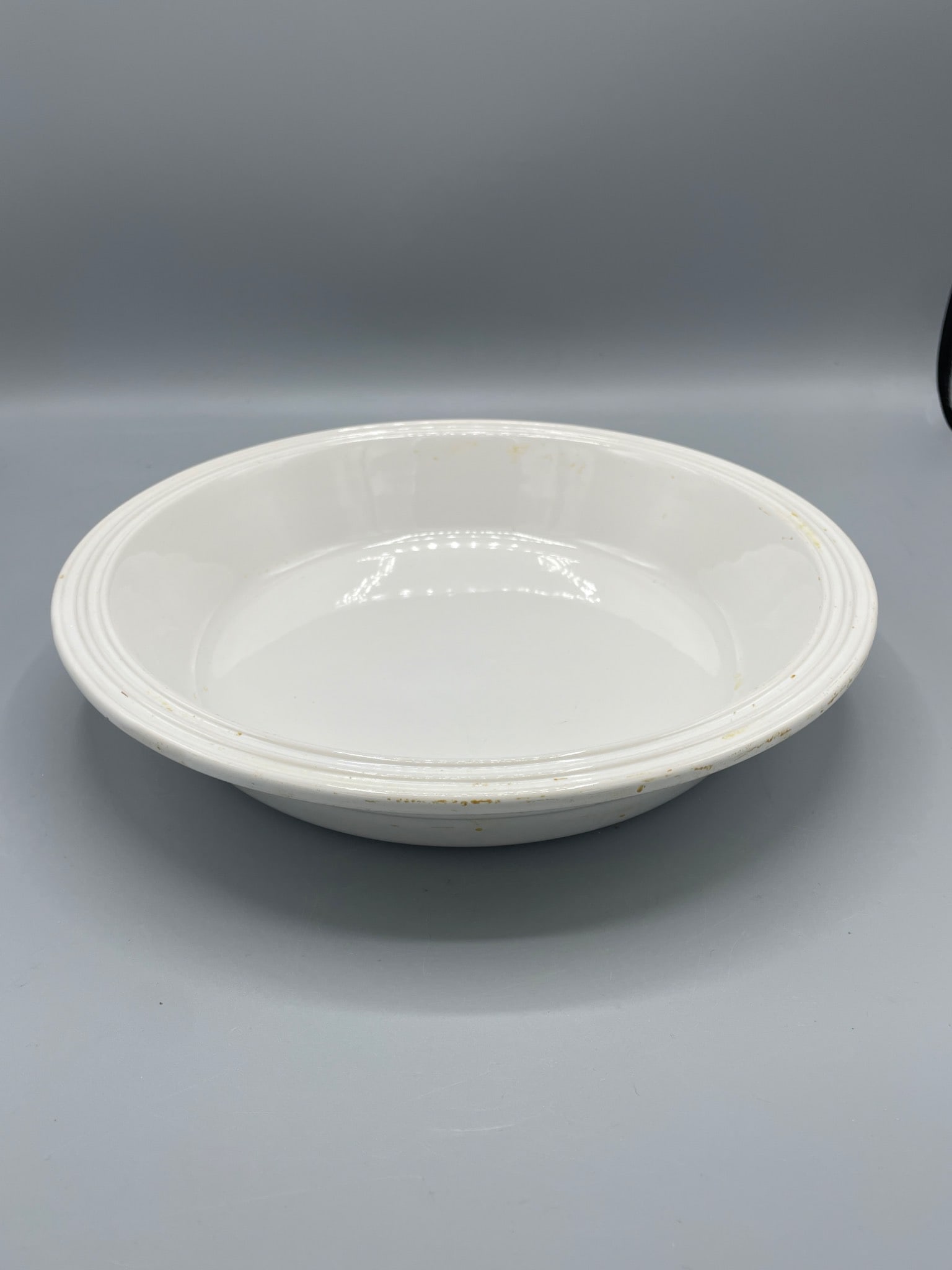 Le Creuset Number 205 White Stoneware Serving Dish: A Le Creuset stoneware serving dish with model number '205' marked on the base. The dish is white with a patterned rim and exhibits signs of surface wear on the underside. Approximate dimensions are