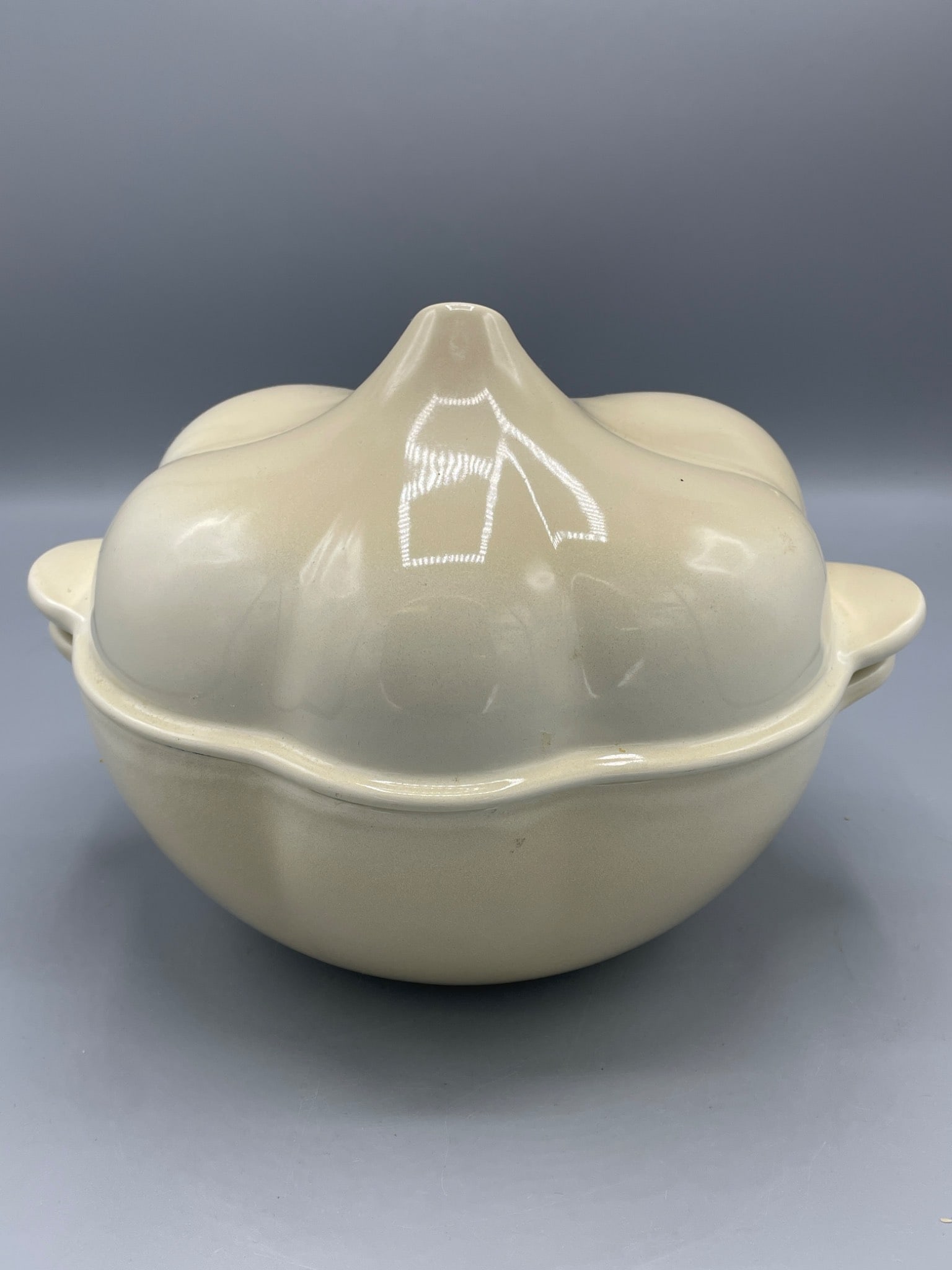 Cast-Iron Garlic-Shaped Casserole Dish, Made in France: This is a cast-iron casserole dish designed in a garlic bulb shape. The exterior is cream-colored with minor rust spots visible, and it features two side handles. Made in France, the interior reveals