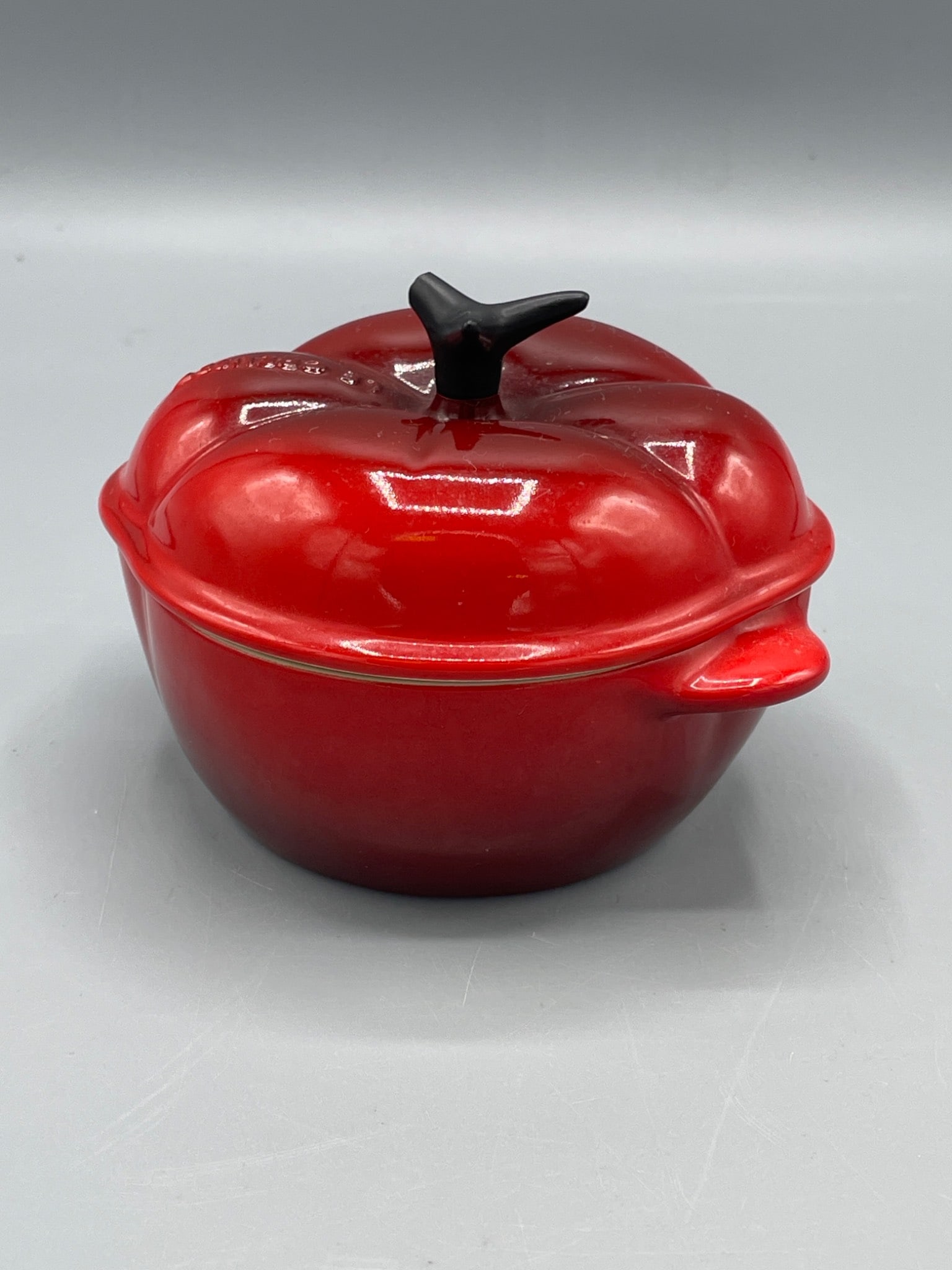 Le Creuset Tomato-Shaped Casserole Dish, Red, Model 0105: Le Creuset ceramic casserole dish in the shape of a tomato, model 0105. Features a vibrant red finish with a black stem-like handle. Made in Belgium, as marked on the base. Includes lid and measures