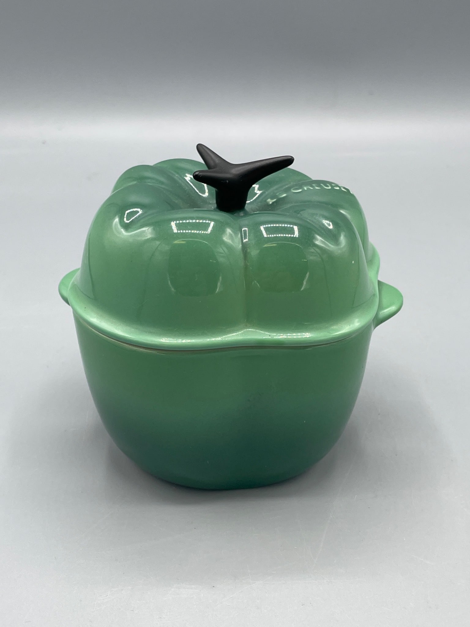 Le Creuset Pepper-shaped Stoneware Casserole Dish with Lid â€“ Model 0105: This listing features a Le Creuset stoneware casserole dish in the shape of a pepper, marked 0105. The exterior is glazed in green with a black stem lid handle, and the interior is beige. The bottom