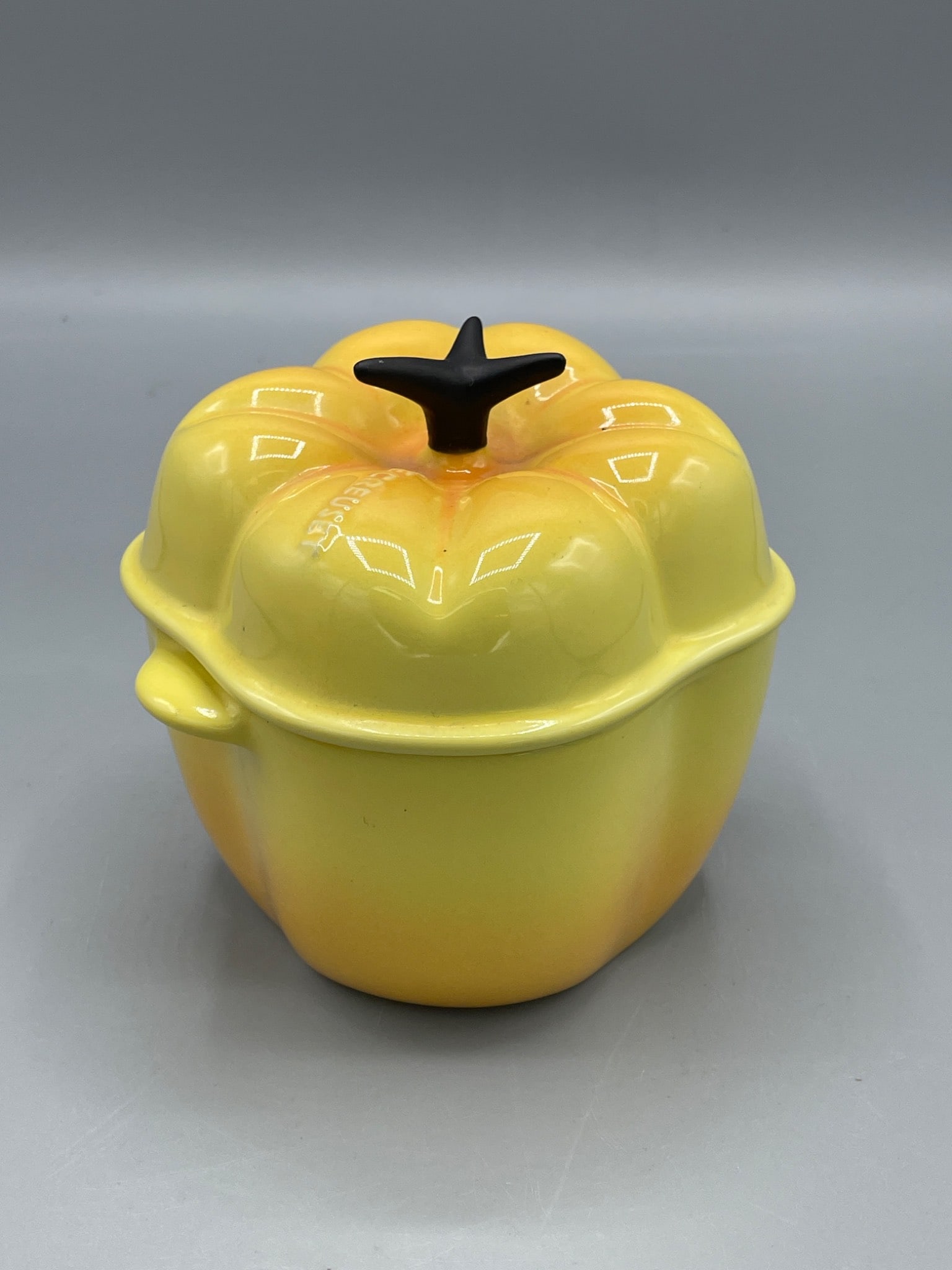 Le Creuset 0205 Ceramic Yellow Bell Pepper Casserole Dish With Lid: Le Creuset ceramic casserole dish in the shape of a bell pepper, featuring a yellow glaze with black detailing on the lid handle. The bottom is stamped with 'Le Creuset' and the model code '0205'.