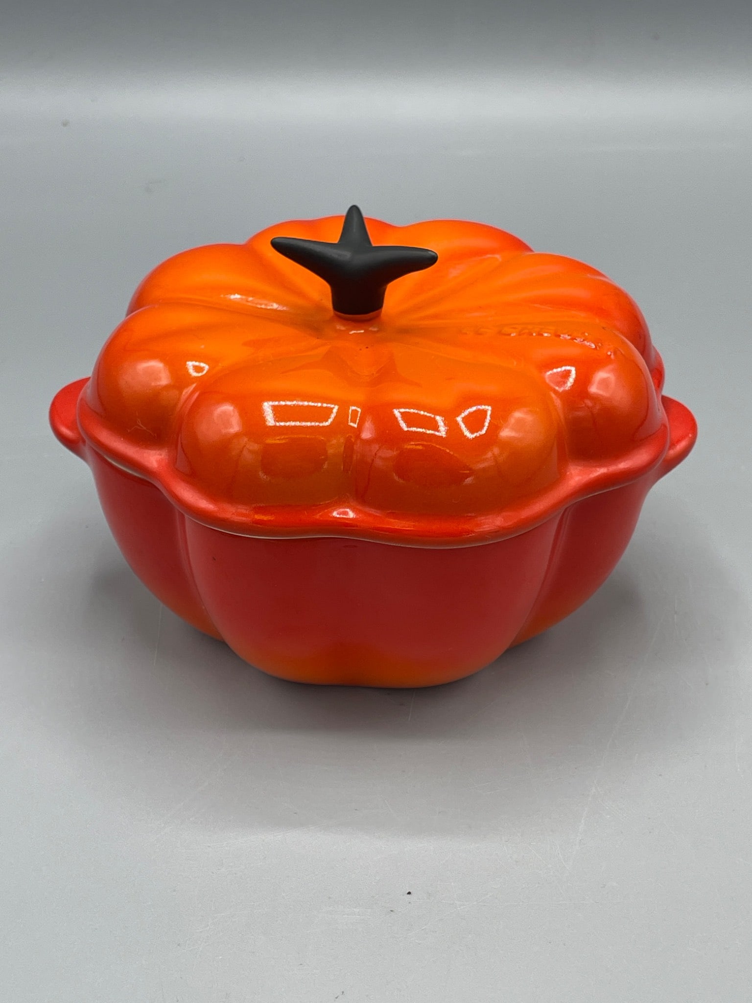 Le Creuset Pumpkin-Shaped Cast Iron Casserole Dish, Marked 0105: Le Creuset pumpkin-shaped cast iron casserole dish, marked 0105. External orange glaze with beige interior enamel and a black knob. Measures approximately 5 inches tall and has a barcode label on the