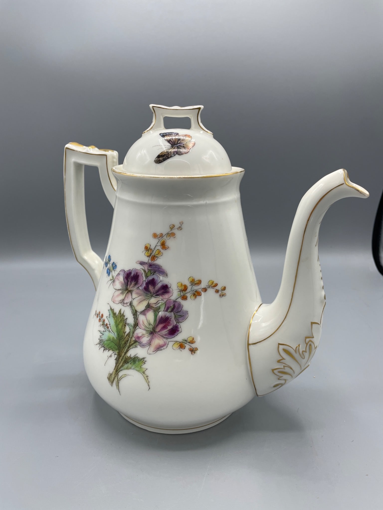 Porcelain Teapot with Floral and Butterfly Design, Approx. 9 Inches Tall: A porcelain teapot featuring floral designs and a butterfly motif on the lid. The teapot measures approximately 9 inches in height. It includes gold-tone accents on the handle, spout, and lid. The