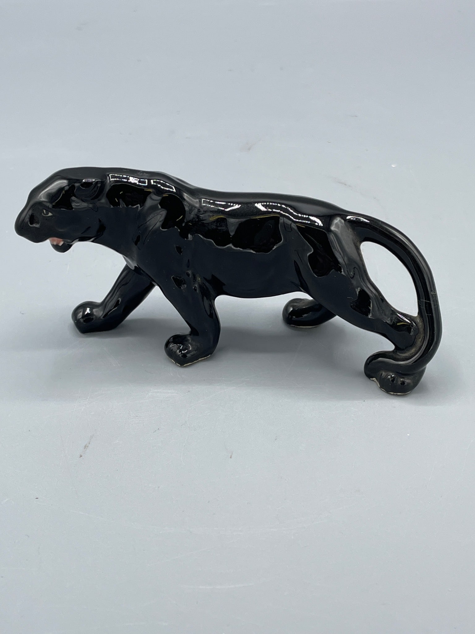 Ceramic Black Panther Figurine with PA Sticker: A ceramic black panther figurine measuring approximately 6 inches in length and 2.5 inches in height. Features a glossy black glaze and a partial label with 'PA' visible on the base. This piece