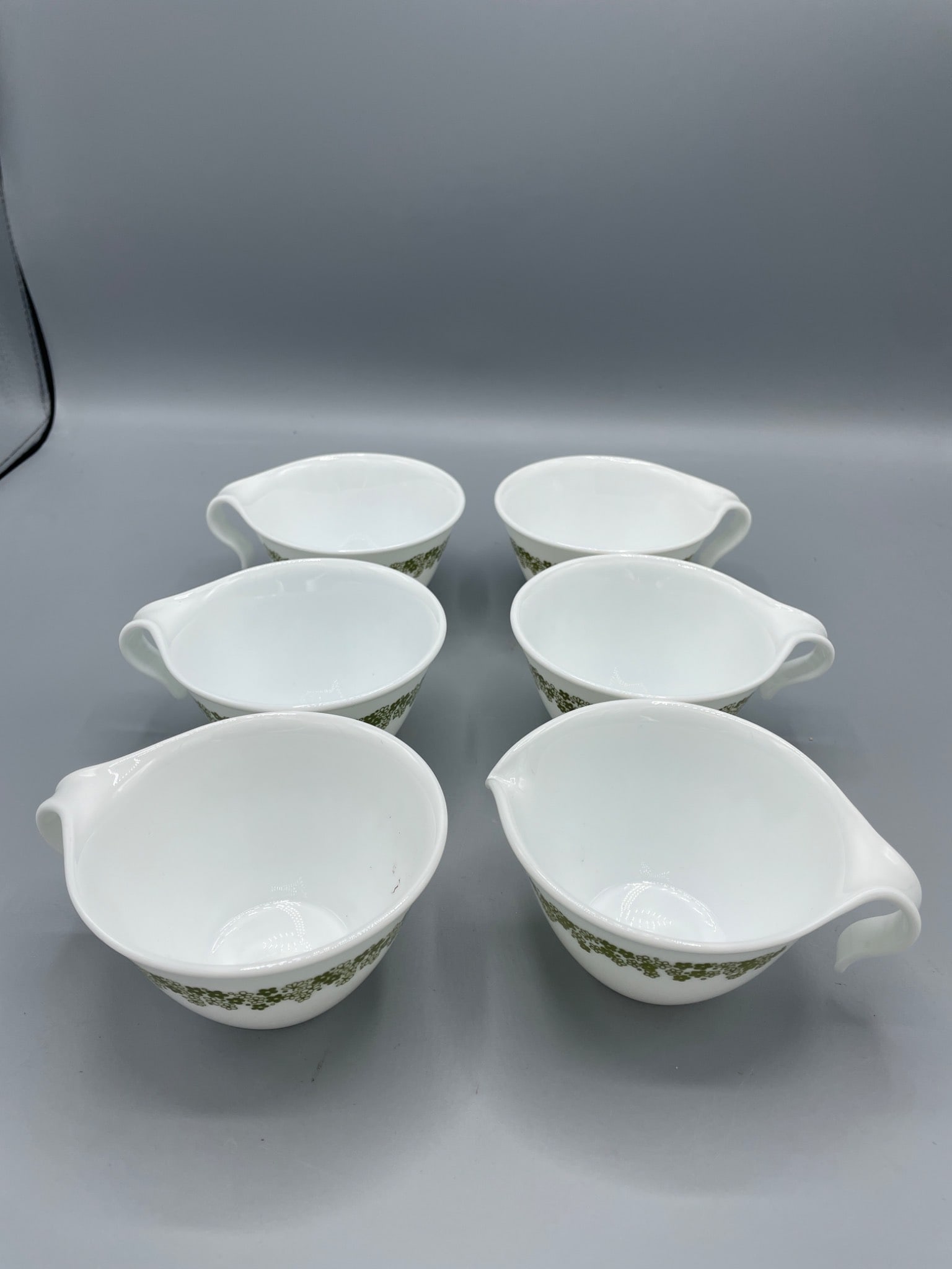 6 Corelle by Corning Creamer Bowls with Green Floral Pattern: This lot contains a set of 6 bowls by Corelle, manufactured by Corning in the USA. The bowls feature a green floral accent design and are marked on the bottom, indicating they are not for broiler or