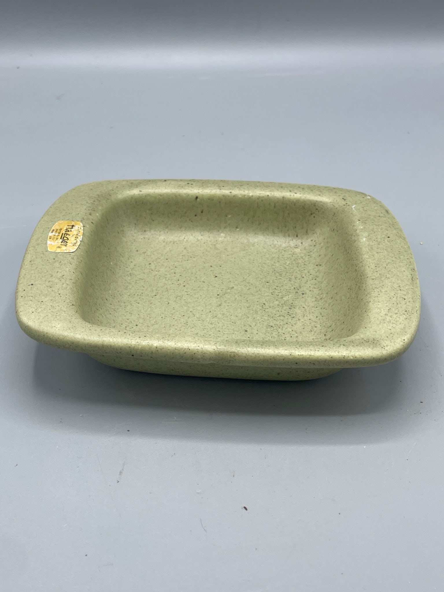 Haeger Potteries Inc. Rectangular Dish, Made in USA: This is a rectangular ceramic dish manufactured by Haeger Potteries Inc. The piece features a speckled green finish and retains its original gold label indicating its origin in the USA. Dimensions