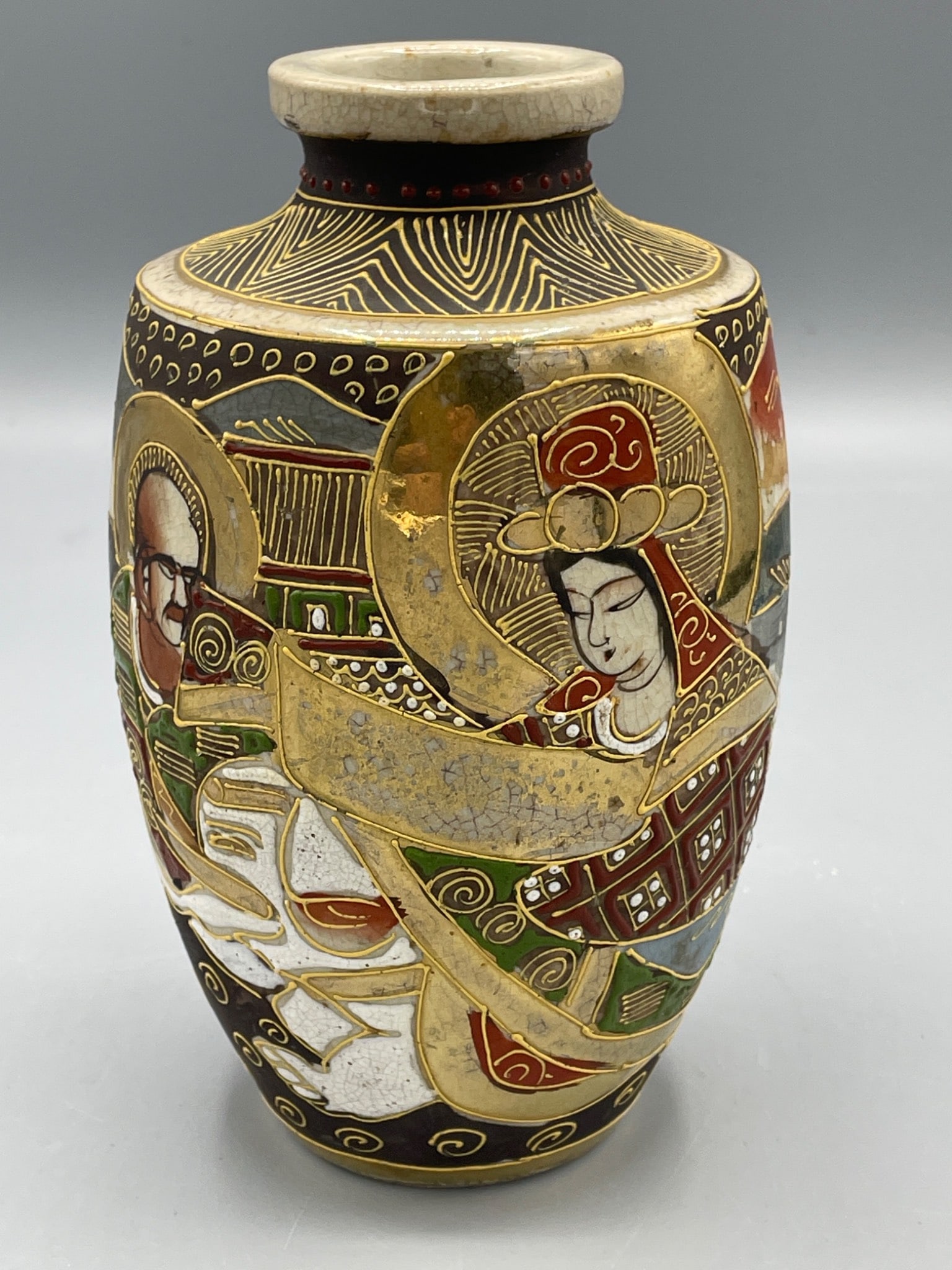 Ceramic Satsuma-Style Vase with Hand-Painted Design and Makers Mark: This ceramic vase features hand-painted designs with gold accents, depicting figures and landscapes. The bottom bears a red makers mark. The piece measures approximately 6.5 inches tall. It reflects