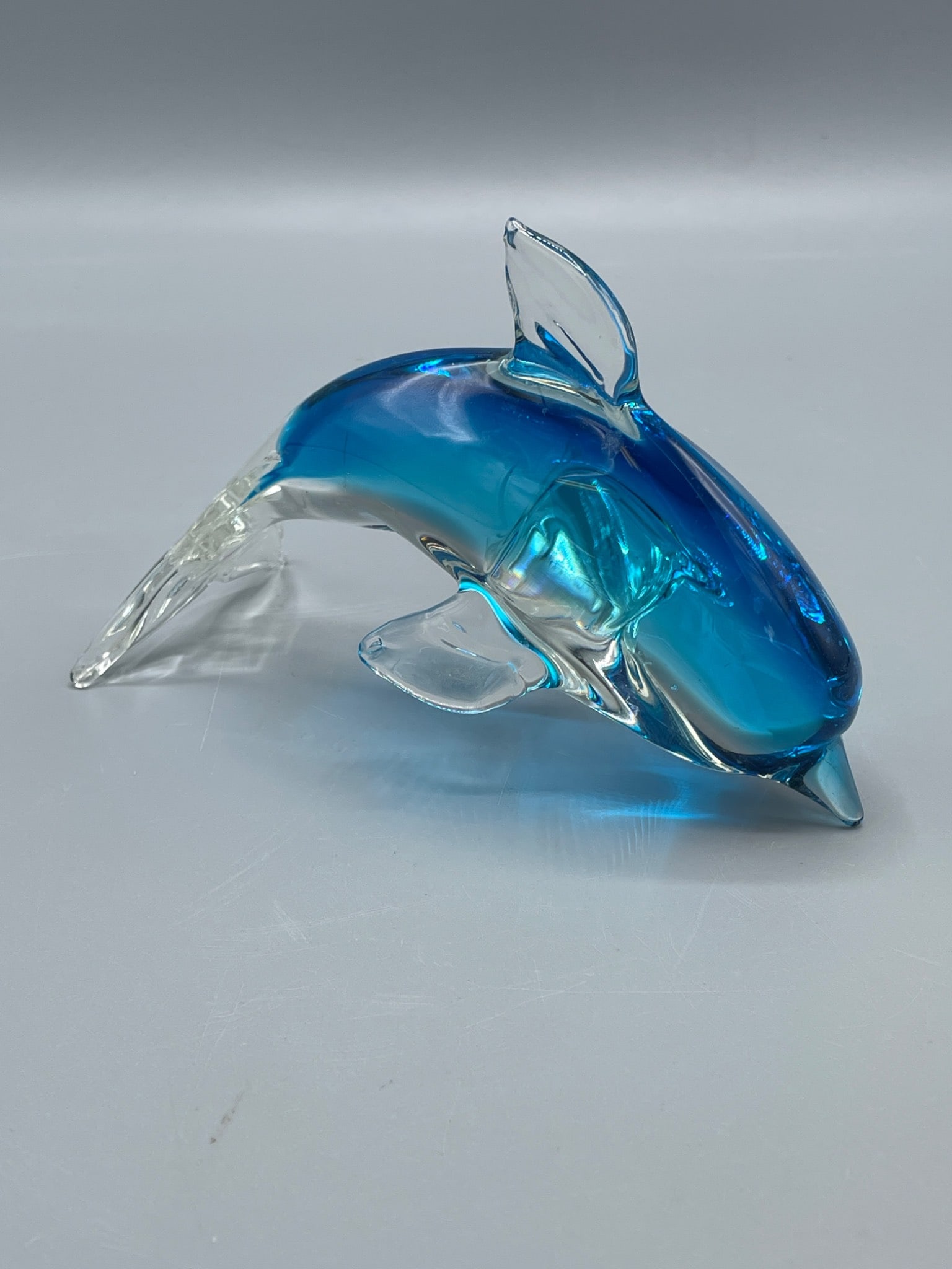 Glass Dolphin Figurine With Blue and Clear Design, Approximately 6 Inches: This is a decorative glass dolphin figurine featuring a gradient blue and clear design. The dimensions of the piece measure approximately 6 inches in length based on the included ruler. The item