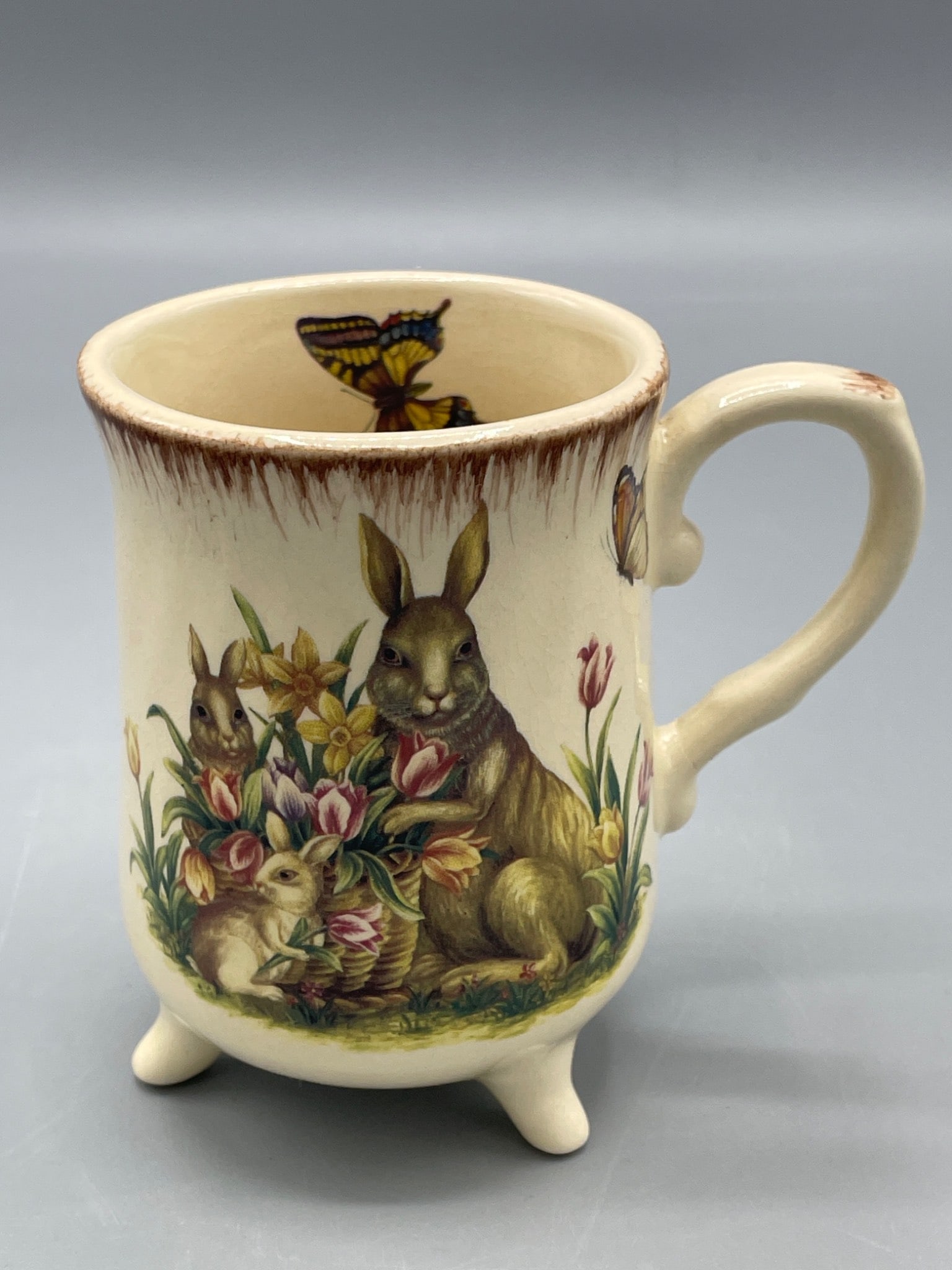 Decorative Ceramic Mug with Rabbit and Floral Motif, Tripod Base: This decorative ceramic mug features a detailed rabbit and floral motif on one side, a floral design on the opposite side, and a butterfly illustrated inside the rim. It stands on three small legs, an