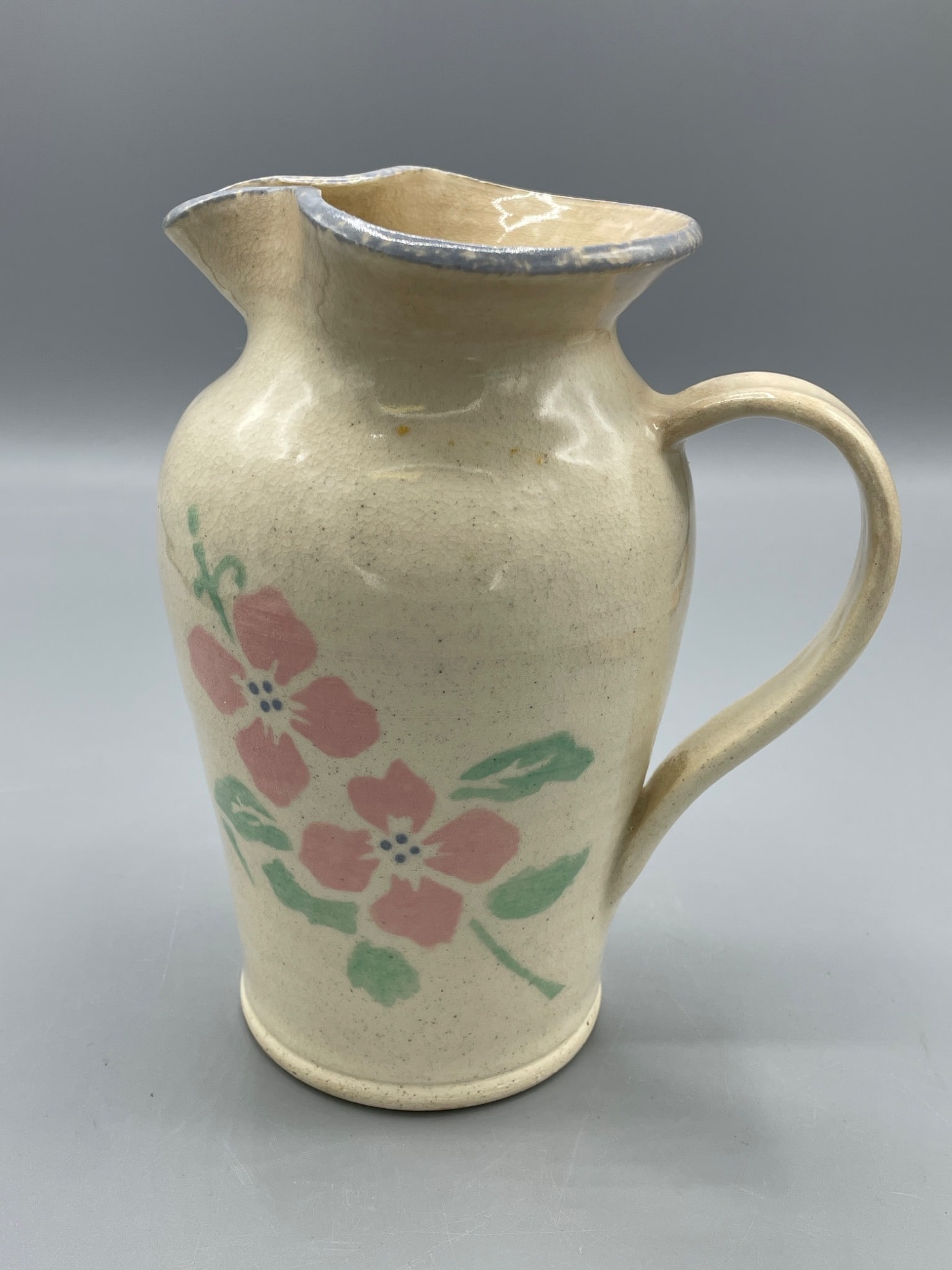 Three Rivers Pottery Ceramic Pitcher, Floral Design, 1989: A ceramic pitcher made by Three Rivers Pottery, dated 1989 as marked on the base. Features a floral design with red and green accents and a blue-gray rim. The pitcher is approximately 6.5 inches tall 