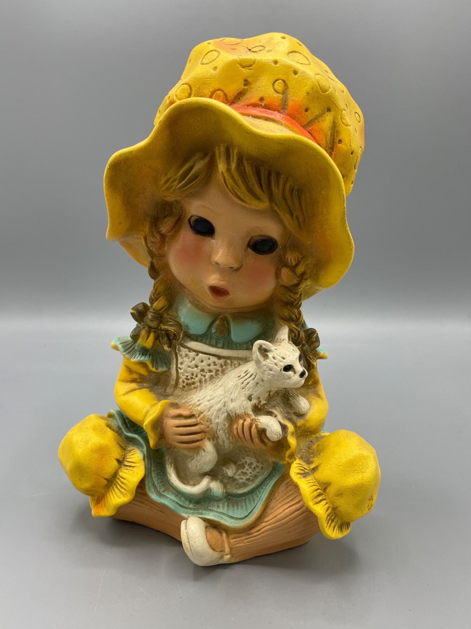 Universal Statuary Figurine of a Seated Girl Hugging a Cat with Yellow Hat: A figurine depicting a young girl in a yellow sun hat and dress, holding a white cat. Measures approximately 9 inches in height. The piece has a felted base for stability. Condition appears good,