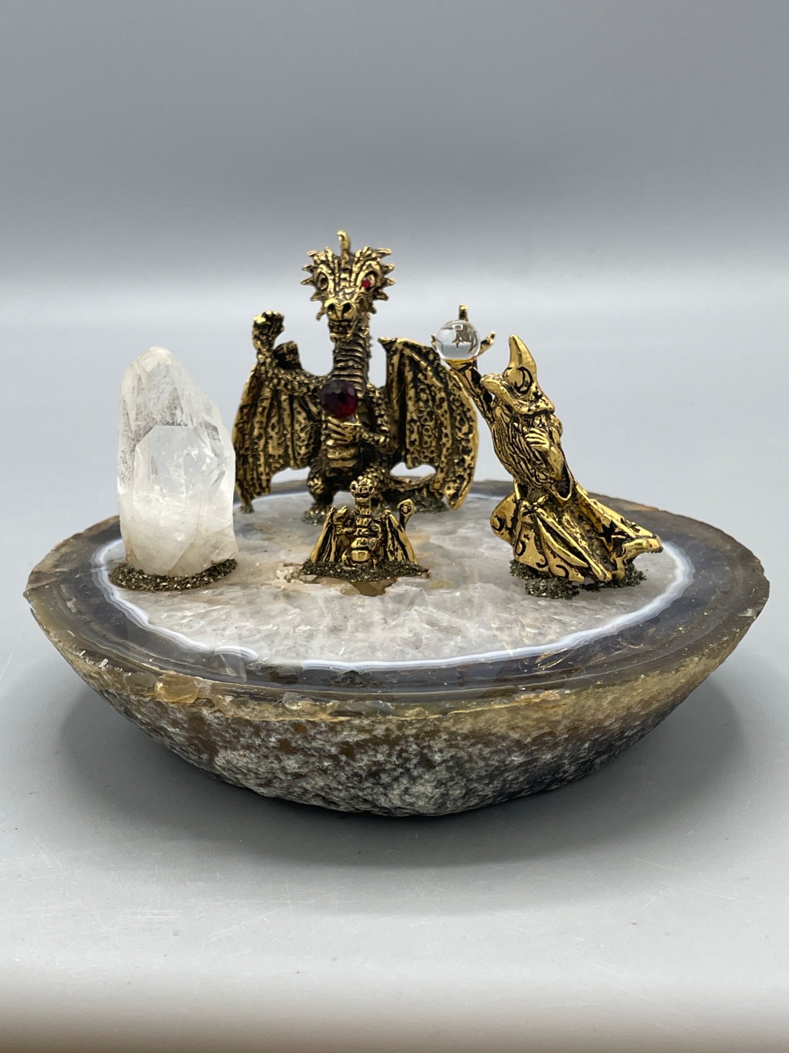 Gold-Tone Dragon And Wizard Figurines On Agate Base With Crystal: This lot features a set of gold-tone dragon and wizard figurines mounted on a polished agate slice base. The dragon and wizard sculptures have embedded faux gem details and a crystal orb accessory.