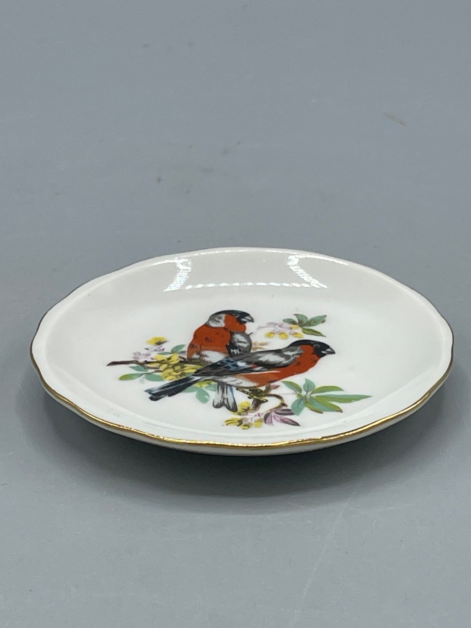 Small Porcelain Plate with Bird Motif, Marked 'Japan': A small porcelain plate featuring a bird motif with floral accents. The plate has a scalloped edge with gold trim, measures approximately 4 inches in diameter, and is marked 'Japan' on the underside.